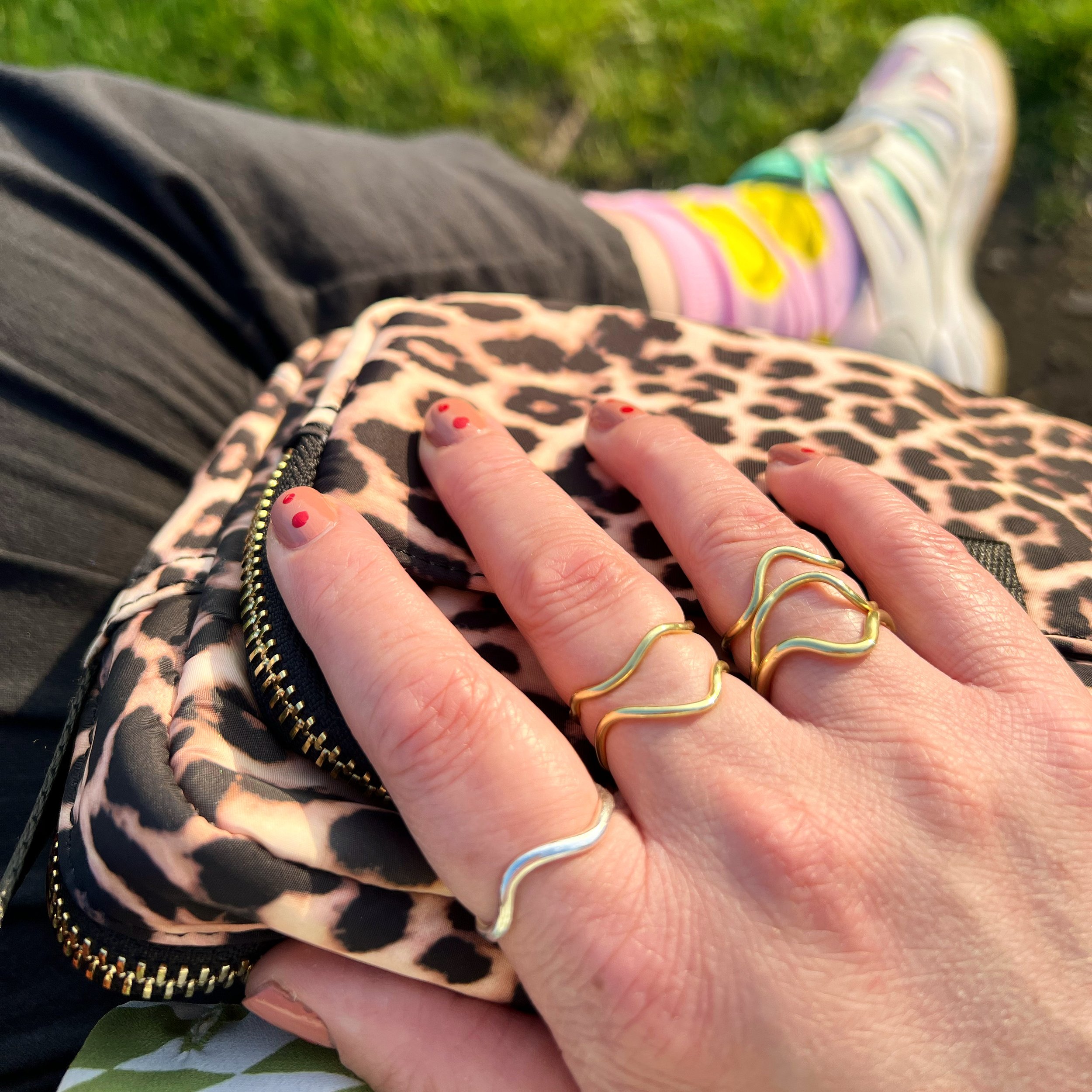  A close-up of a hand on a leopard print bag. The hand is adorned with 6 wiggly rings. 