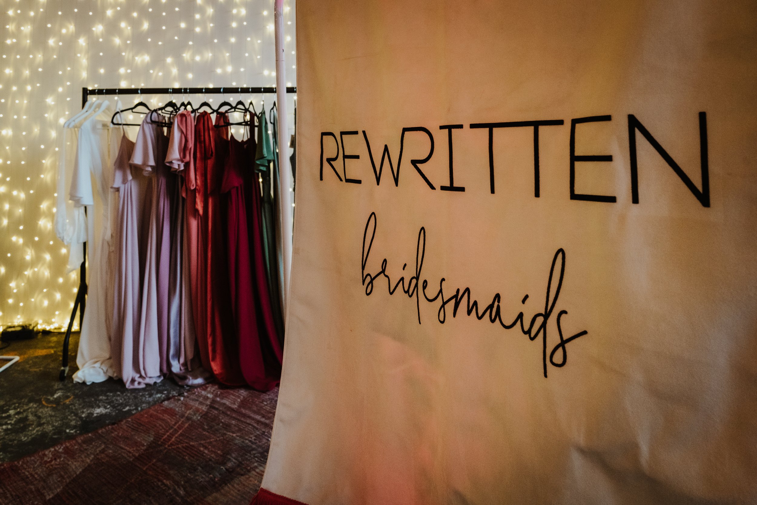 A rail of colourful bridesmaid dresses and a canvas sign in the forefront that says Rewritten Bridesmaids. 