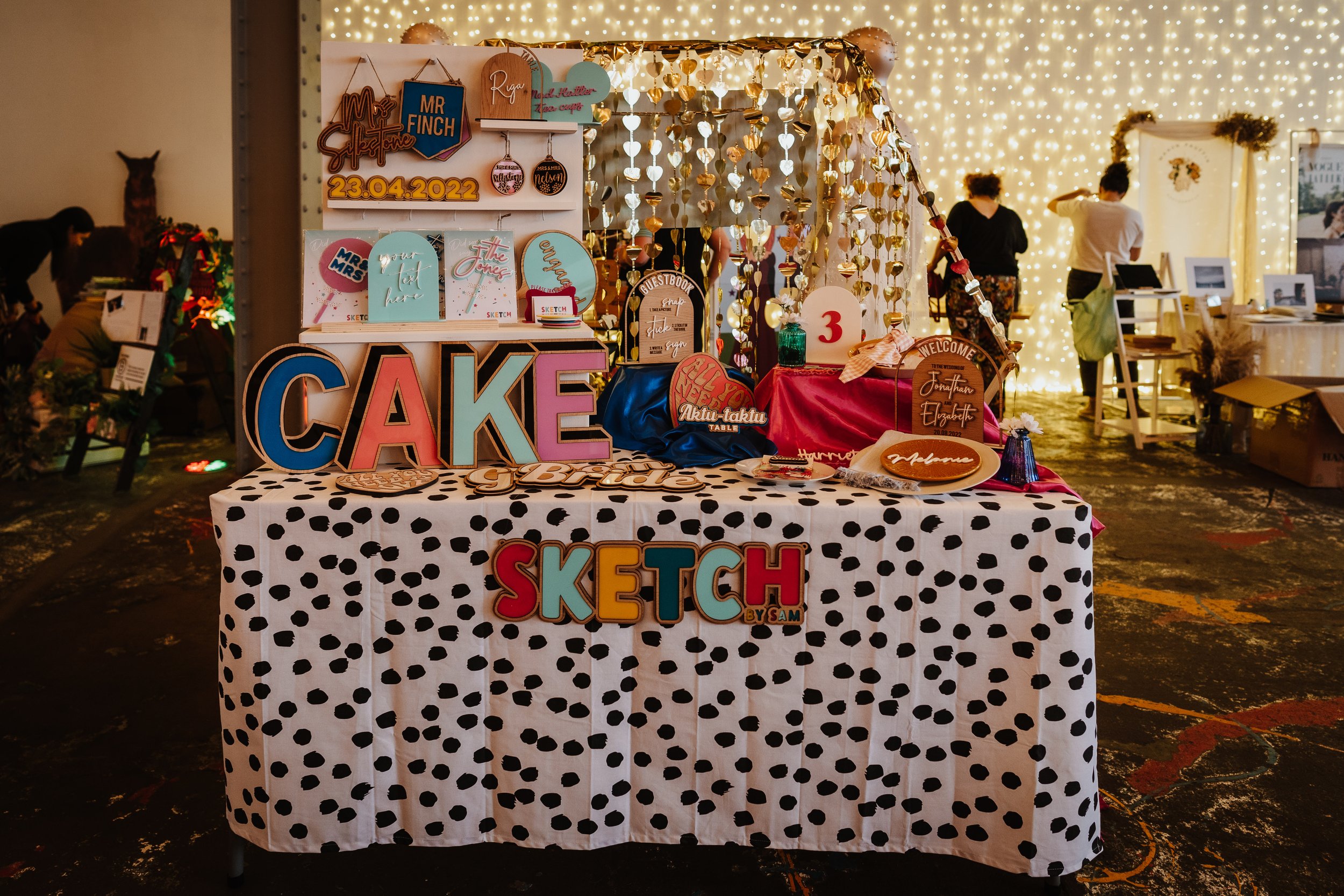  A colourful supplier stand at The Un-Wedding Show  featuring hand made signs and large cut out letters that say CAKE. 