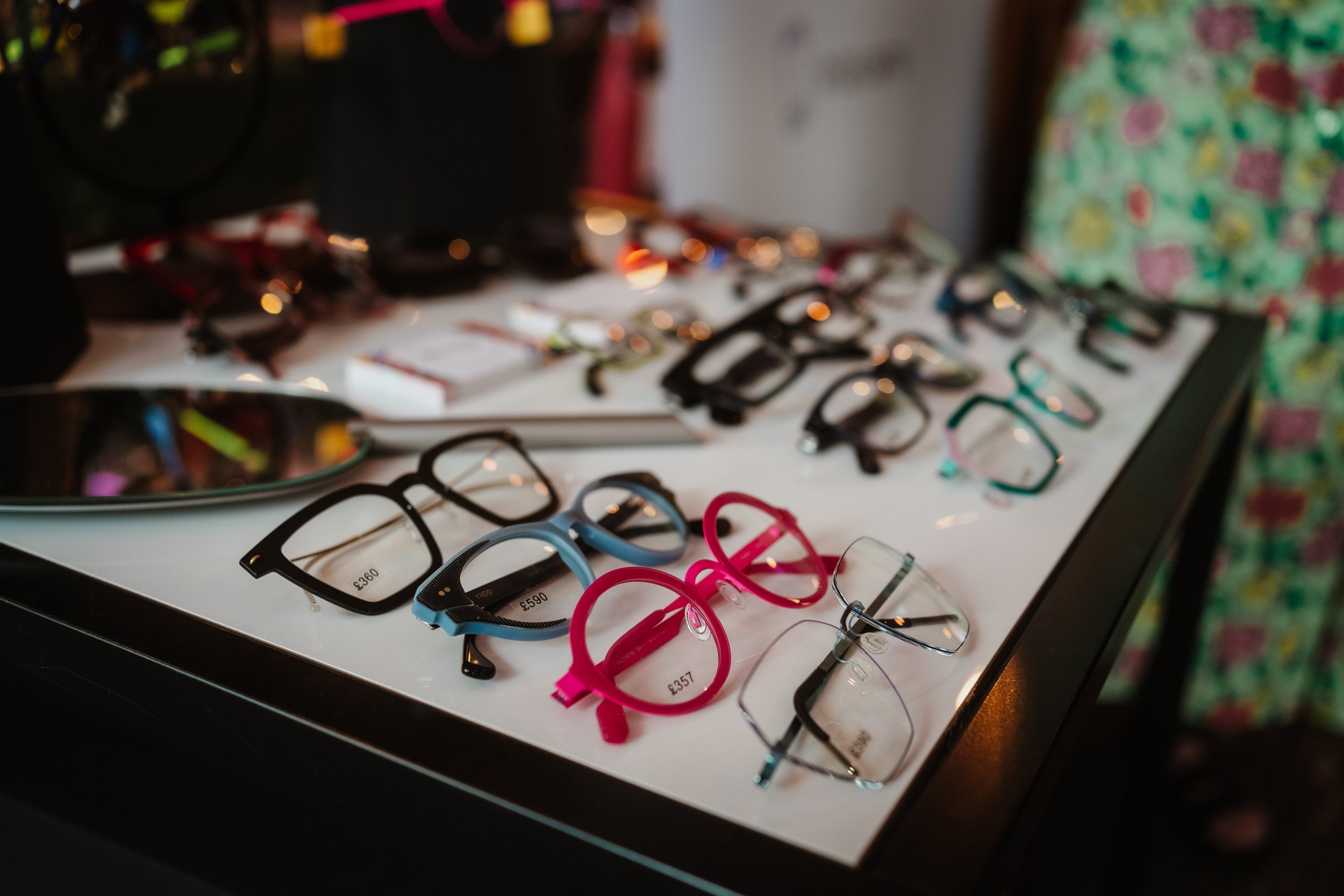  A white table with lots of colourful designer glasses frames. 