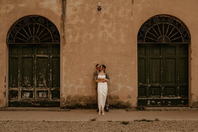  An artistic shot od a bride and groom posing against a peach wall with 2 large black ornate door arches on either side of them. 
