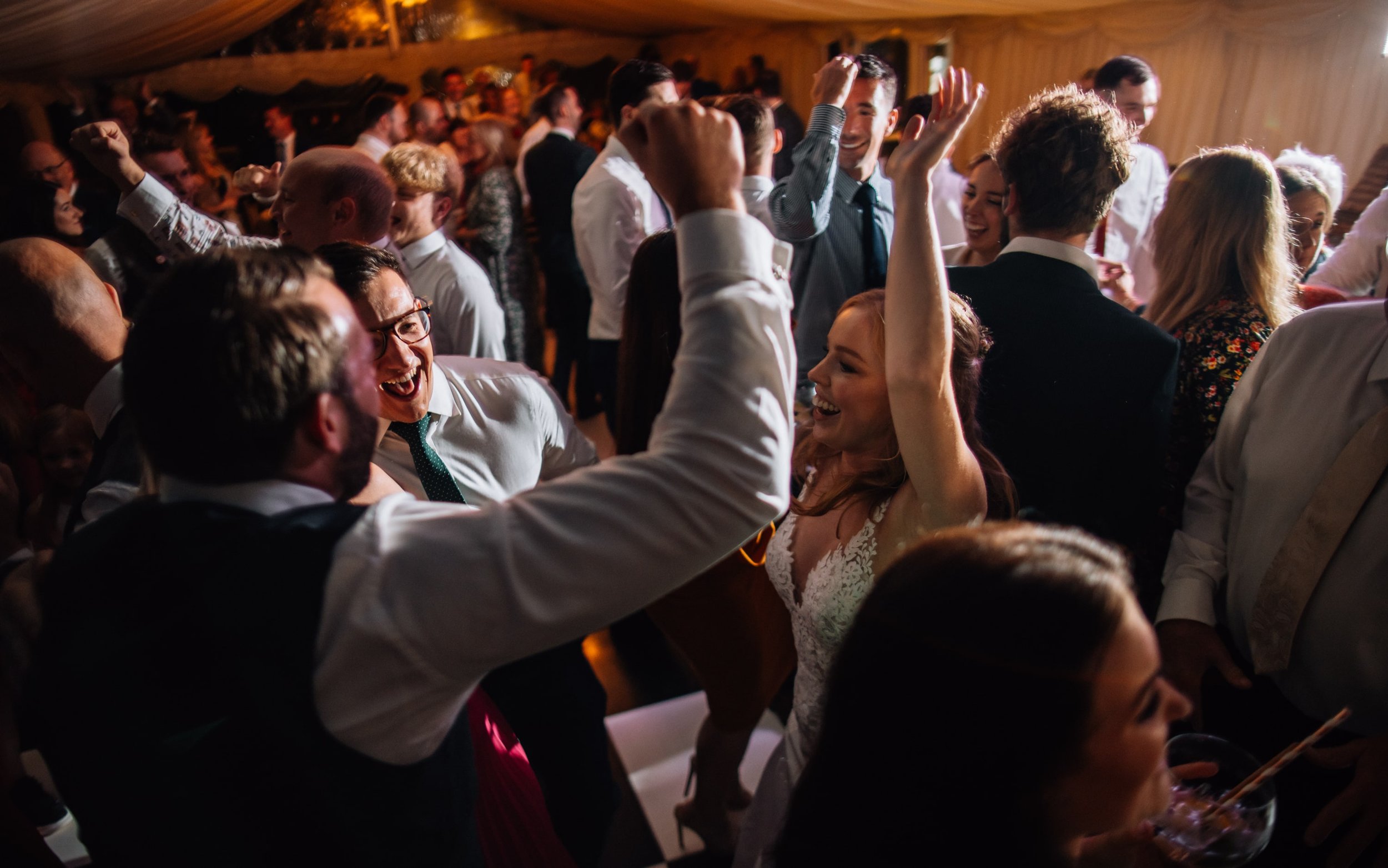  A bride dancing with her guests at her wedding. They all have their arms in the air. 