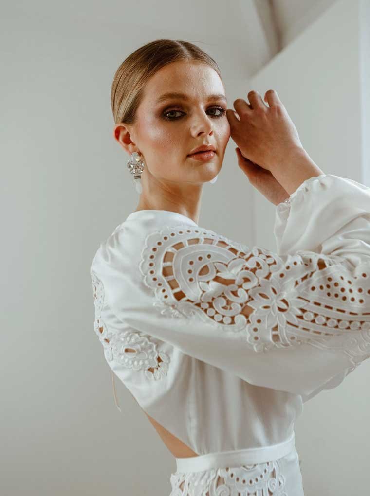  An editorial image of the top half of a blonde bride wearing a long-sleeved wedding dress with lace details. 