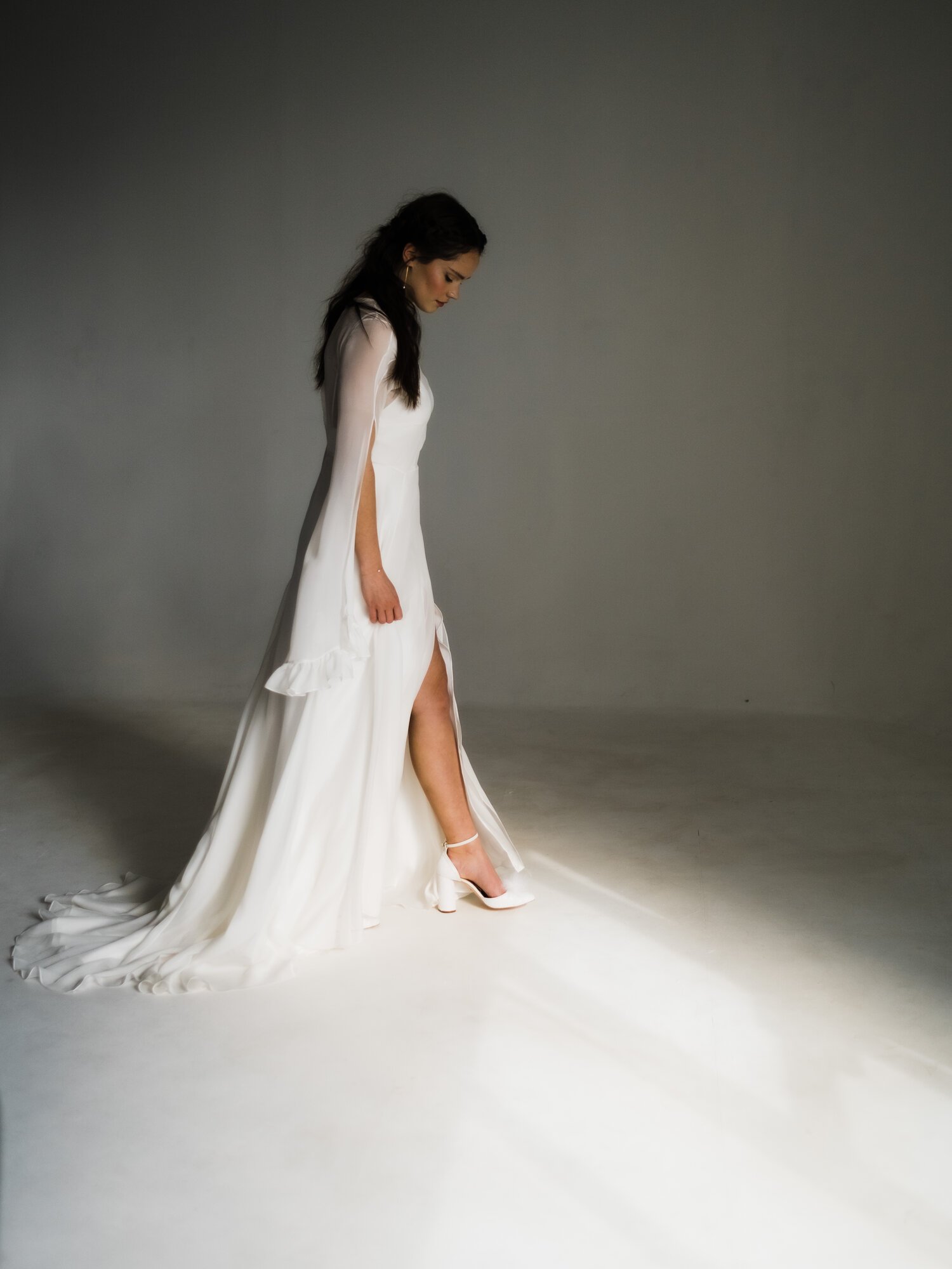  A dark haired bride stands side on to the camera in a long white gown with a split in the front. 