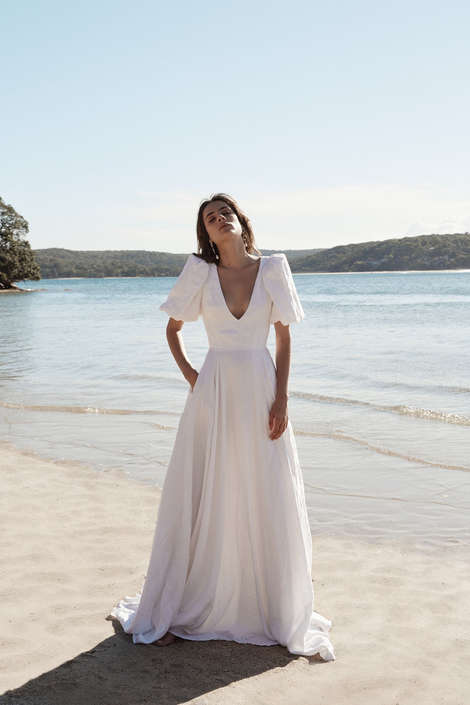  A bride standing on a beach wearing a long white wedding dress. 