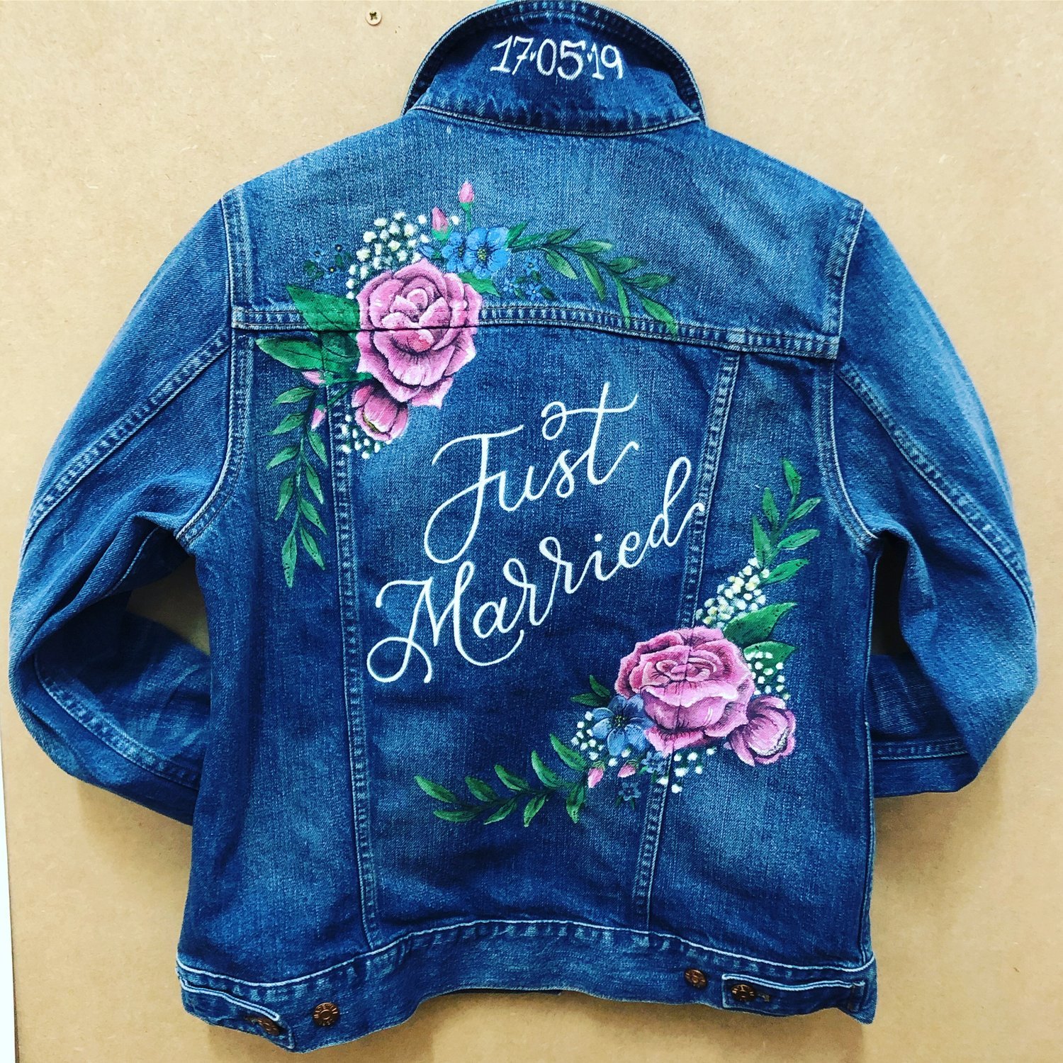  A blue denim jacket with the date painted in white under the collar and ‘Just Married’ painted in white calligraphy across the back. Above to the left and below to the right of ‘Just Married’ pink roses have been hand painted. 