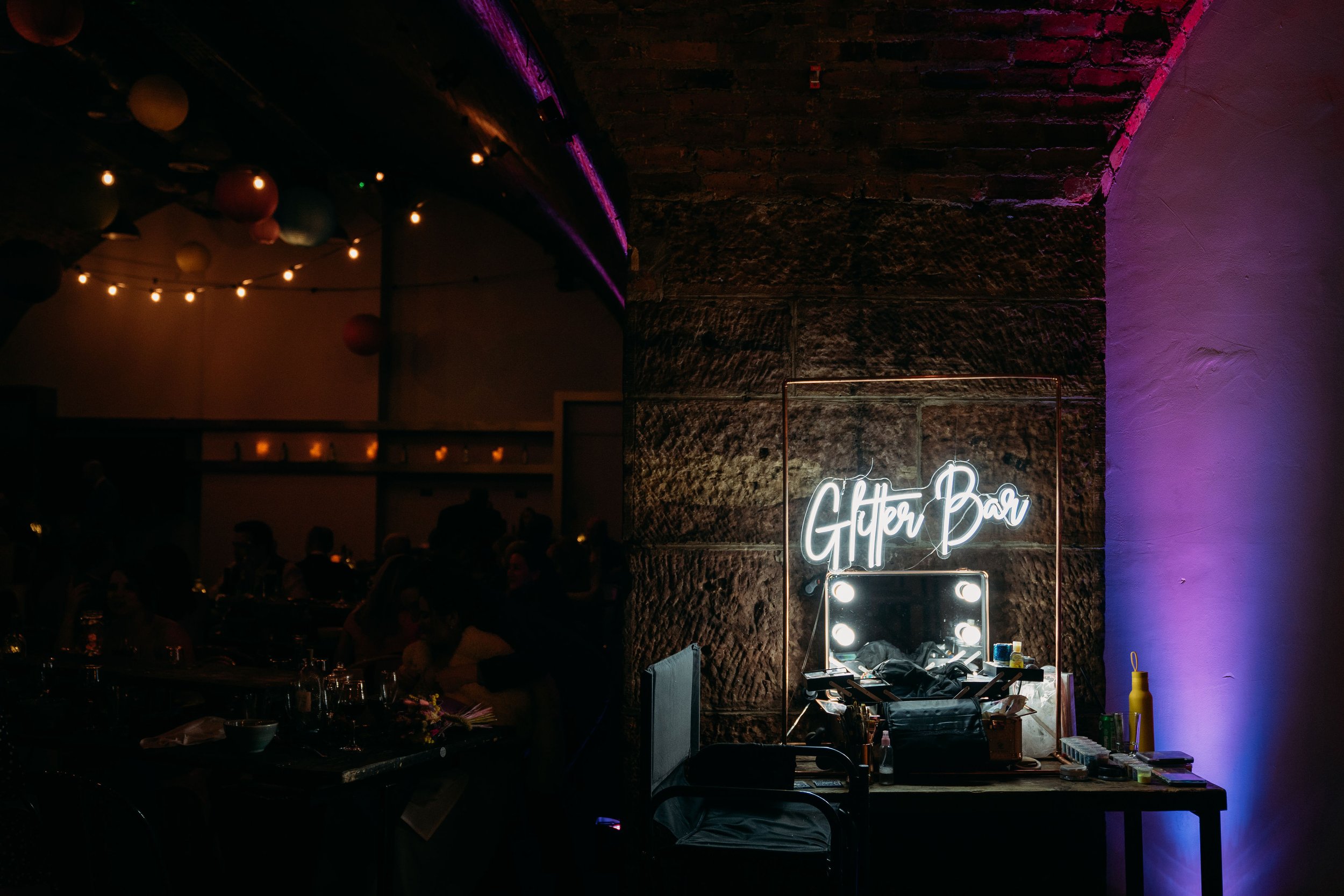  Beautiful shot of the Glitter Bar set up at an evening wedding reception. A neon sign saying Glitter Bar is within a copper frame that highlights the seating area to the side and make up in front.  Photo credit: Jo plus Liam @jodonaldsonphotography 