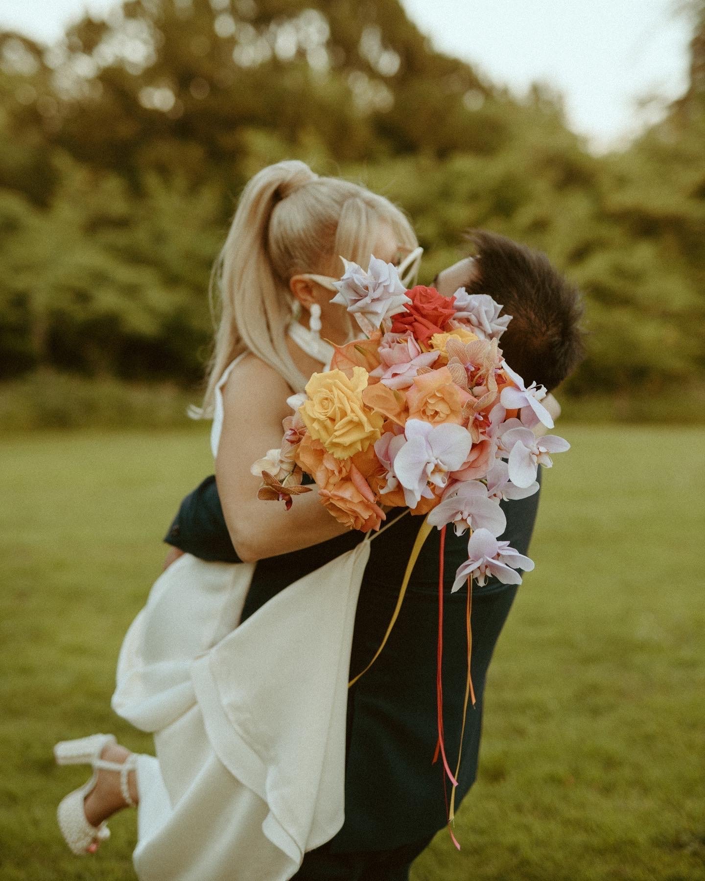  Taken outside the bride is being lifted up by the groom and the couple share a kiss which is discreetly hidden by the brides stunning hand tied bouquet. The large bouquet is made up of lots of large roses in creams, pinks, peach and orange with the 