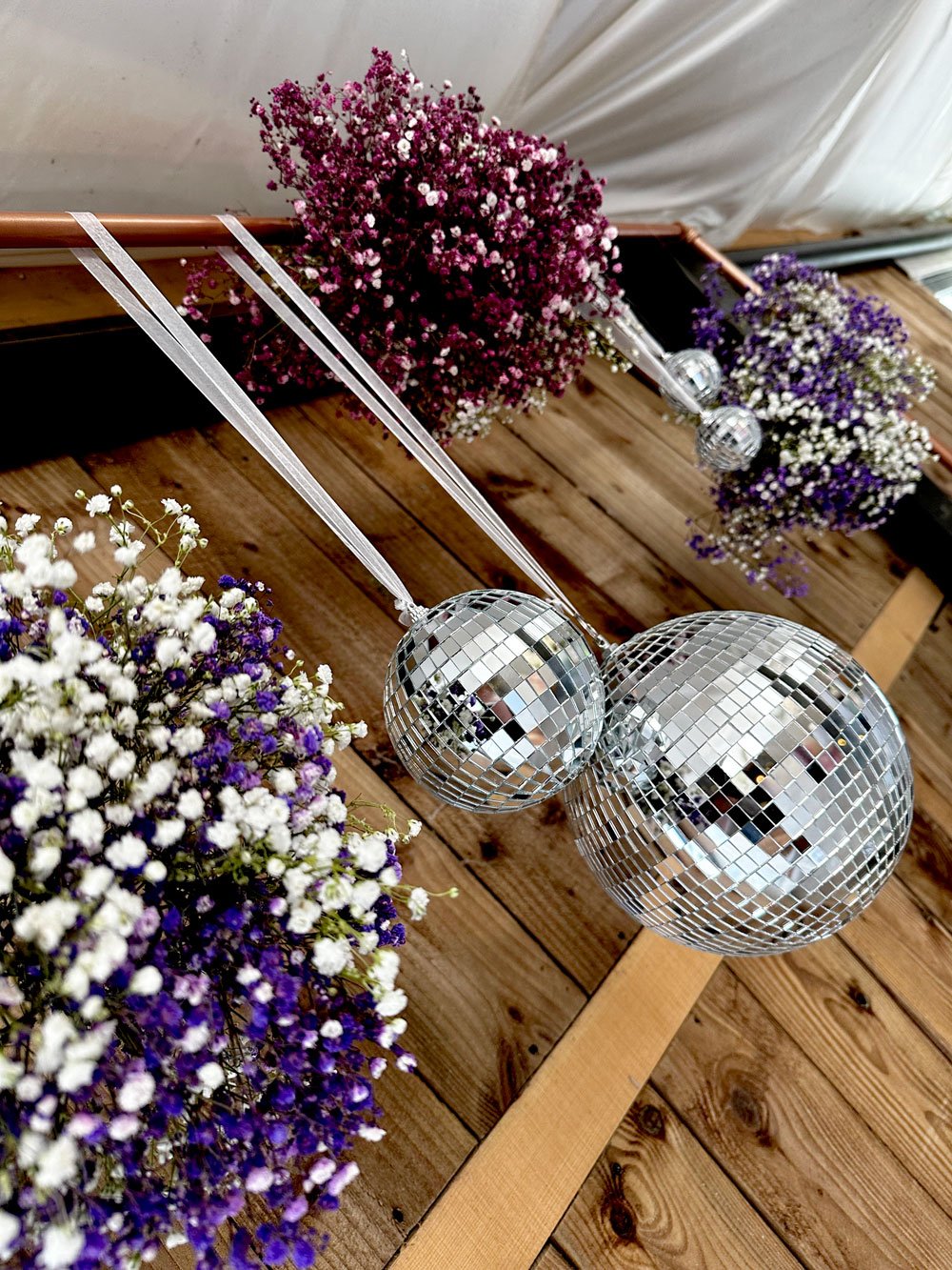  Two beautiful balls of purple and white flowers and one ball of pink and white flowers hang alongside glitter balls to create a stylish and modern floral display. 