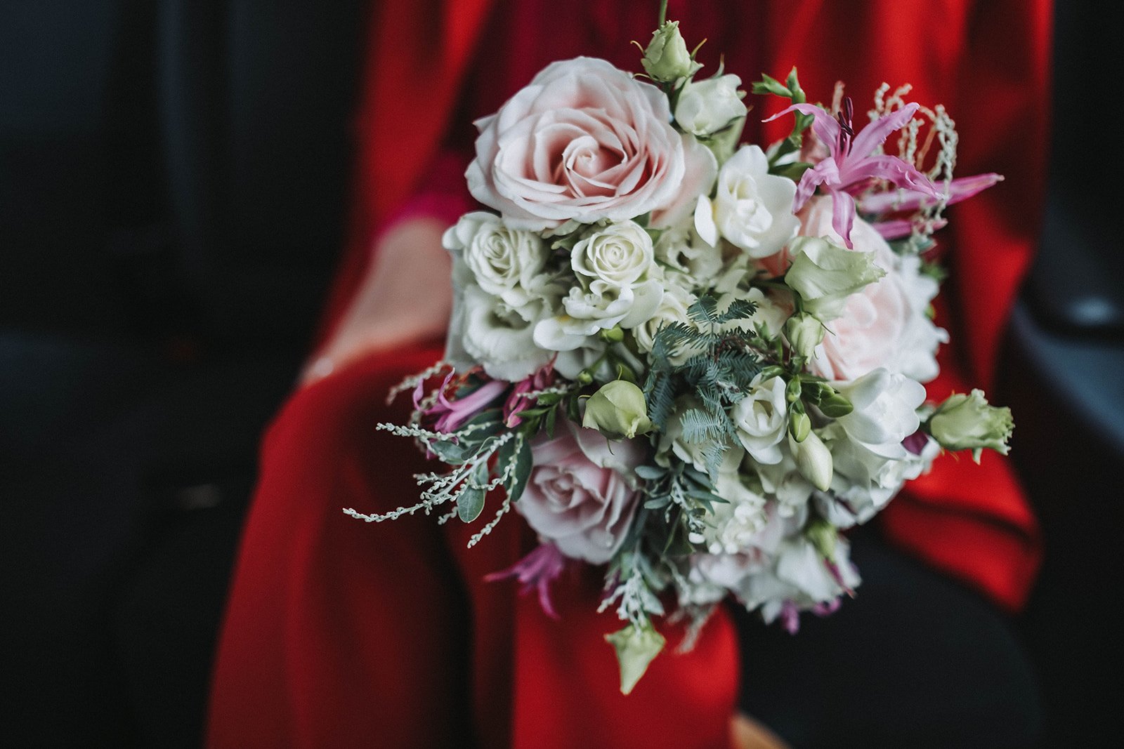  A close up image of a beautiful pink and white hand tied wedding bouquet. The red outfit of the person holding the wedding florals is blurred in the background. 
