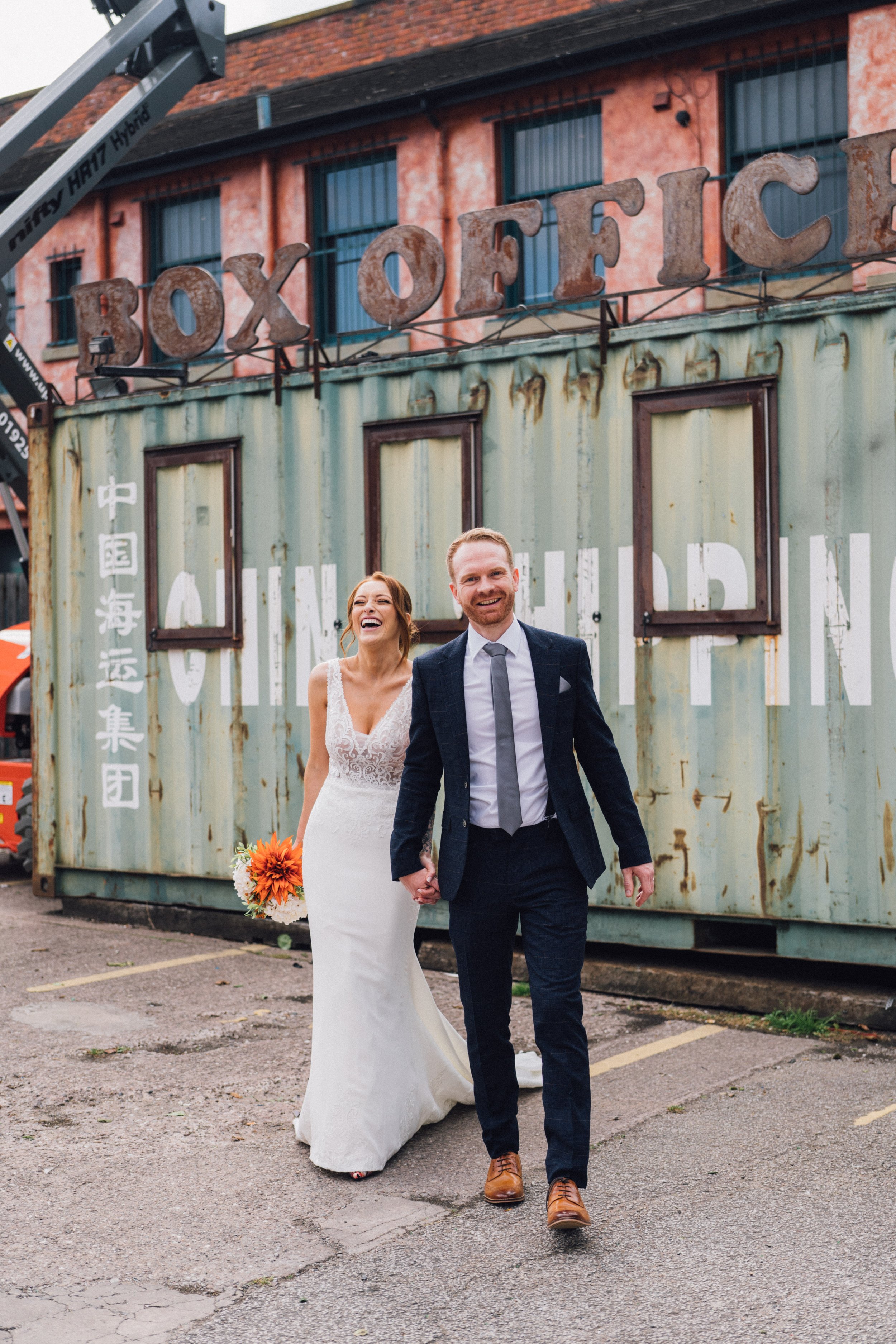  Photographer Credit: Alexandra Holt Photography  Bride and groom are stood outside the Victoria Warehouse wedding venue in front of the old BOX OFFICE. The rusty looking sign above the green shipping container looks very cool, and is a lovely contra