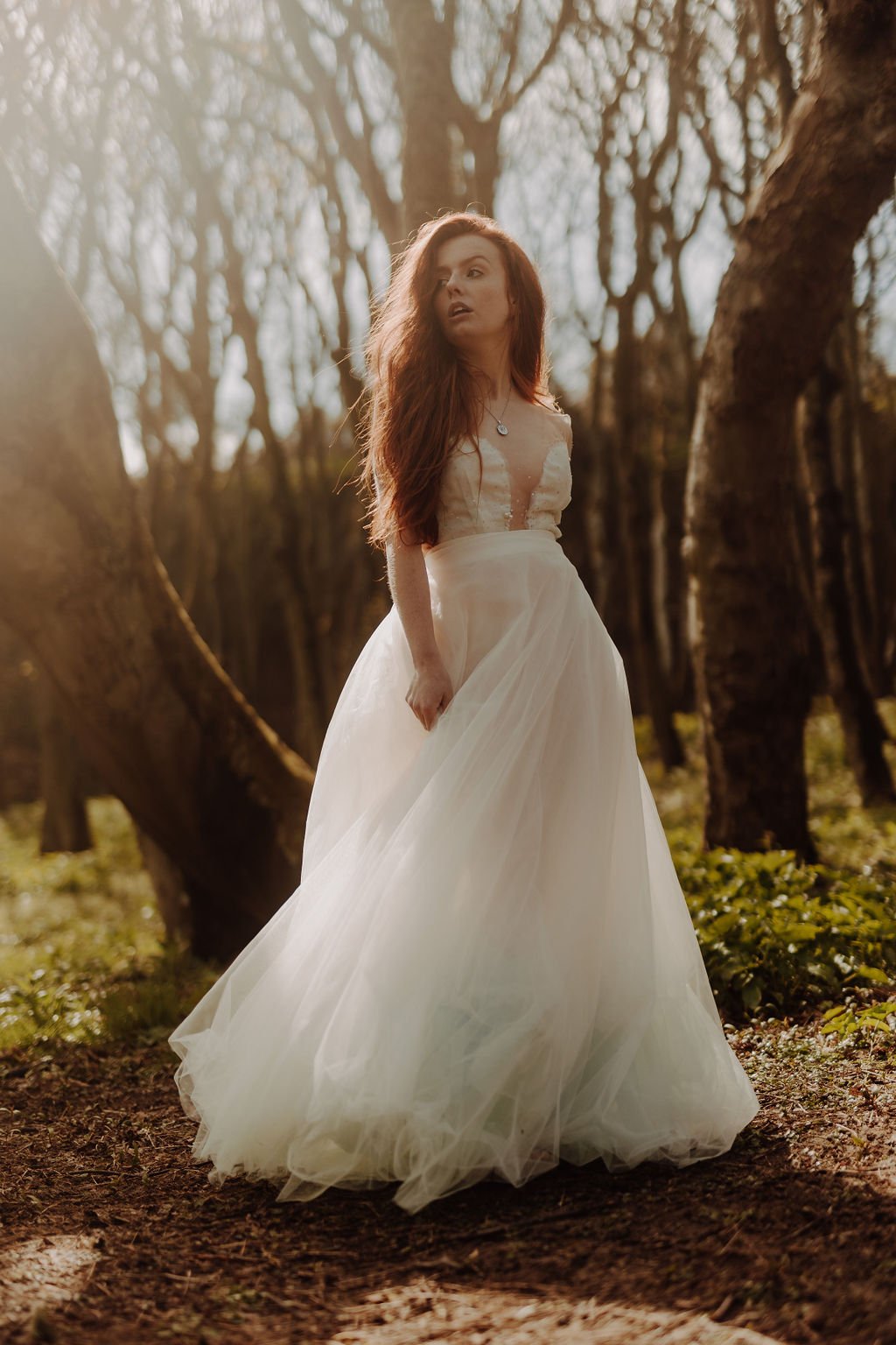 Stood in a forest the bride is wearing a timeless wedding dress with cut out top and full skirt.