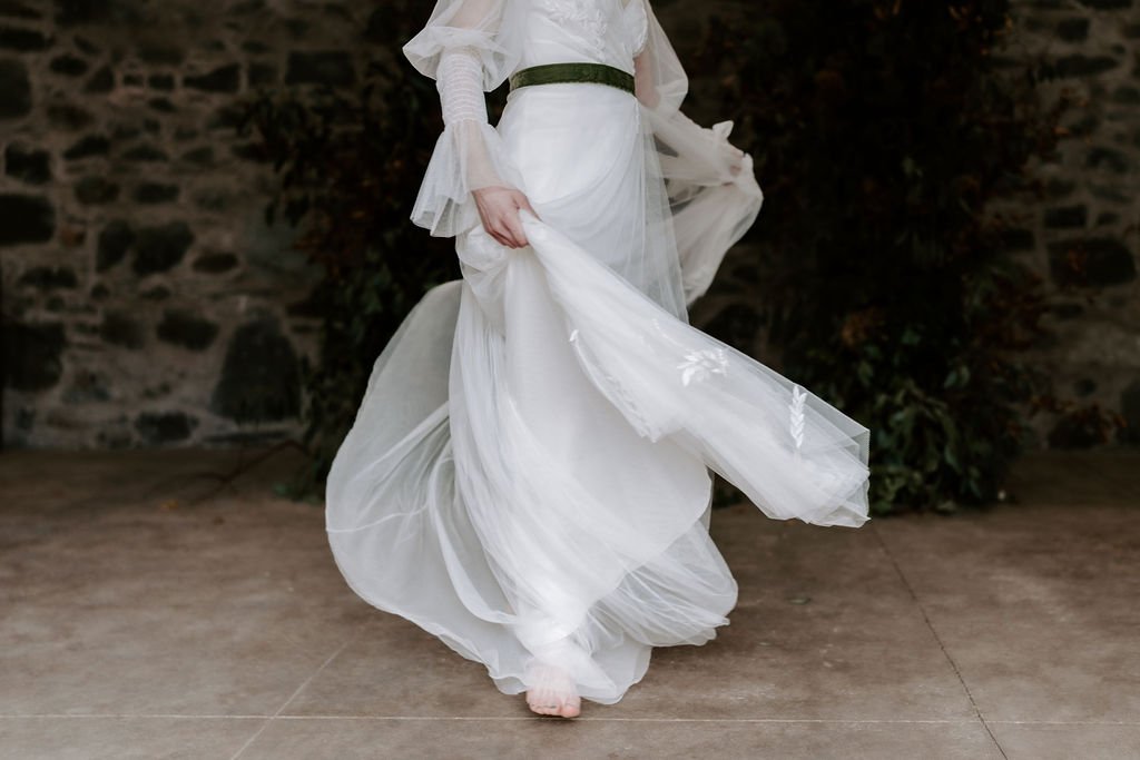 Romantic, hand-crafted full skirt, long white wedding dress with long sleeves and a narrow black waistband belt.