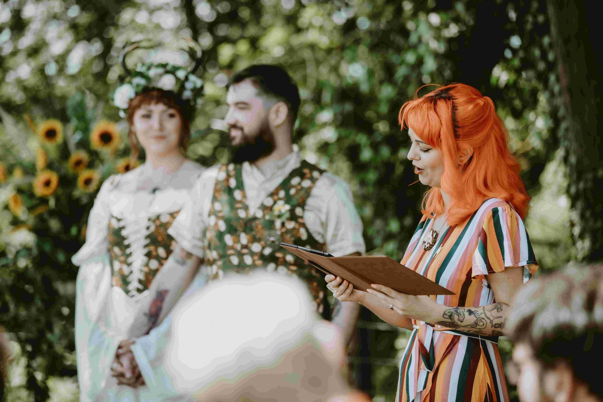  Photo by: Christopher Terry Photography  A close up image of the modern humanist wedding celebrant mid-ceremony nreading from her folder whilst the bride and groom are stood to the side of her looking back out towards their wedding guests. The cool 