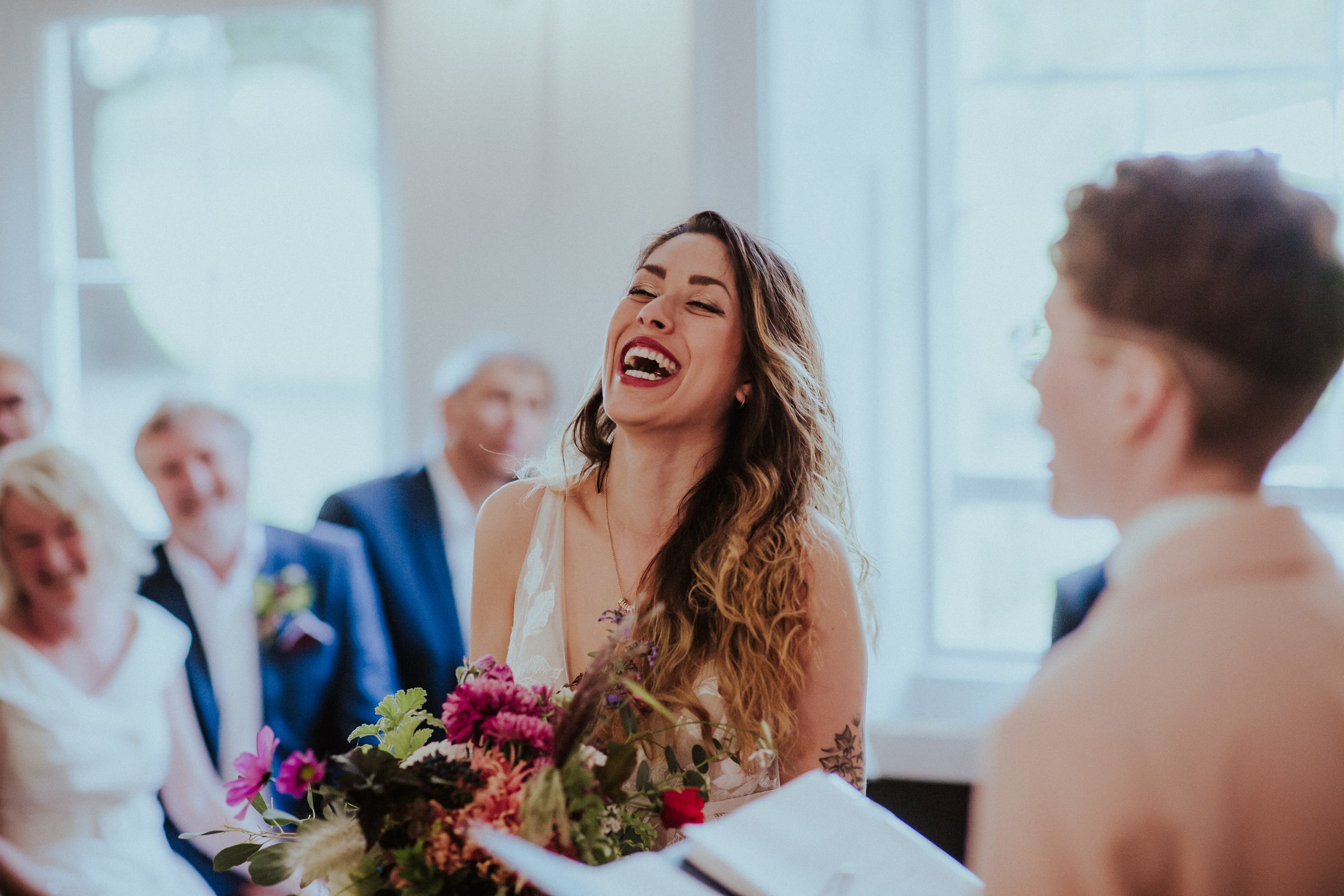  Bride is photographed laughing as she reacts to a funny part in the wedding ceremony crafted by the cool, modern celebrant who can be seen blurred at the forefront of the image.   Photo by: Steven Haddock Photography 