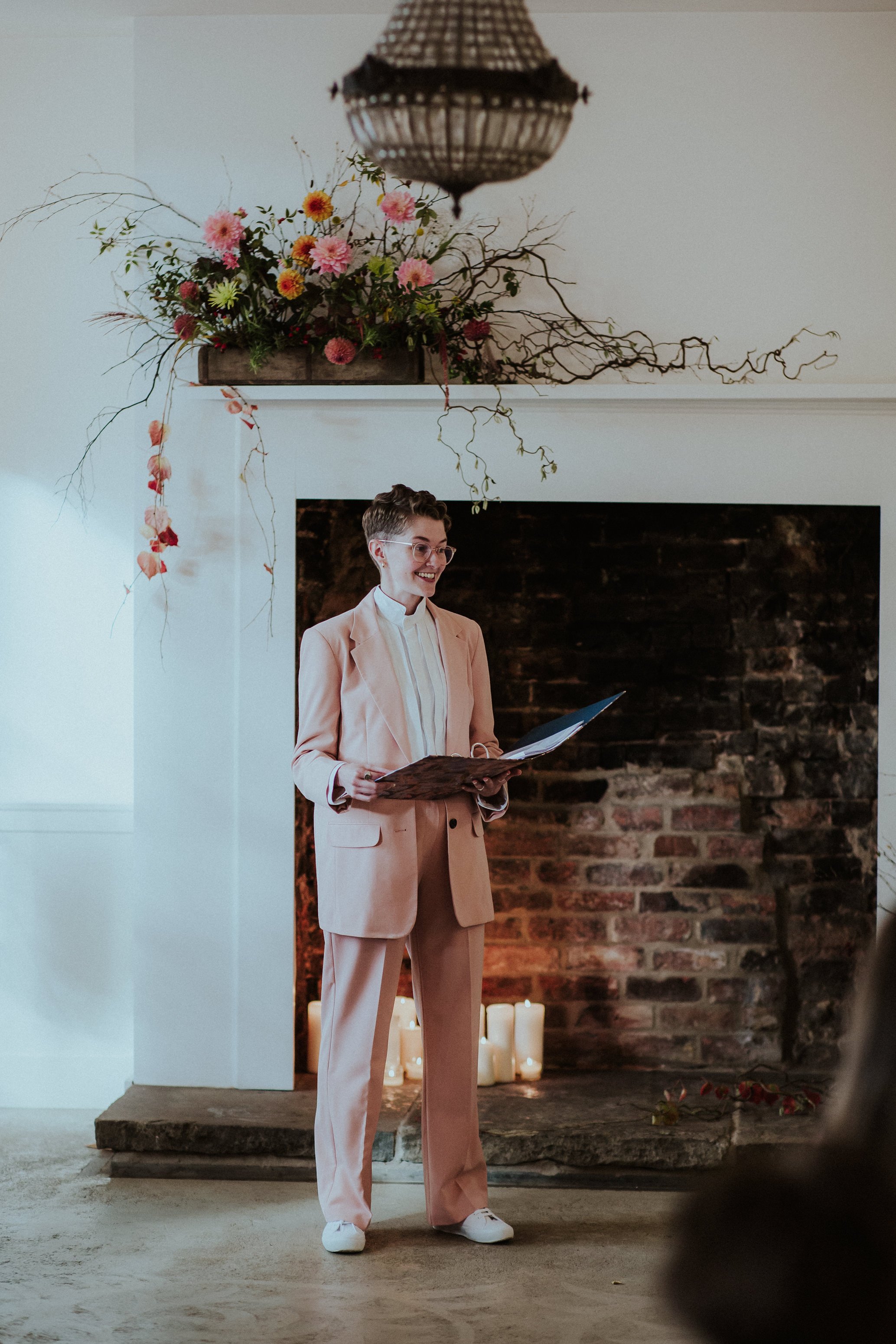  A natural shot of the celebrant delivering her bespoke wedding ceremony full of warmth and laughter to the brides and their wedding guests. She is wearing a beige suit, white shirt and white trainers.  Photo by: Steven Haddock Photography 