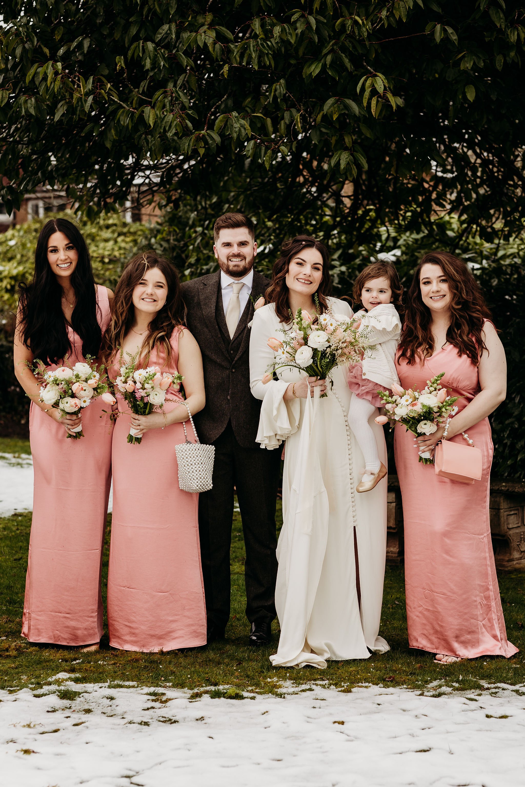  Beautiful wedding florals compliment the bridal party’s bridesmaid dresses, the bride’s wedding dress and the groom’s tie and  complete the floral wedding look. The bride and bridesmaid’s are all stood holding the pink and cream hand tied bouquet’s 