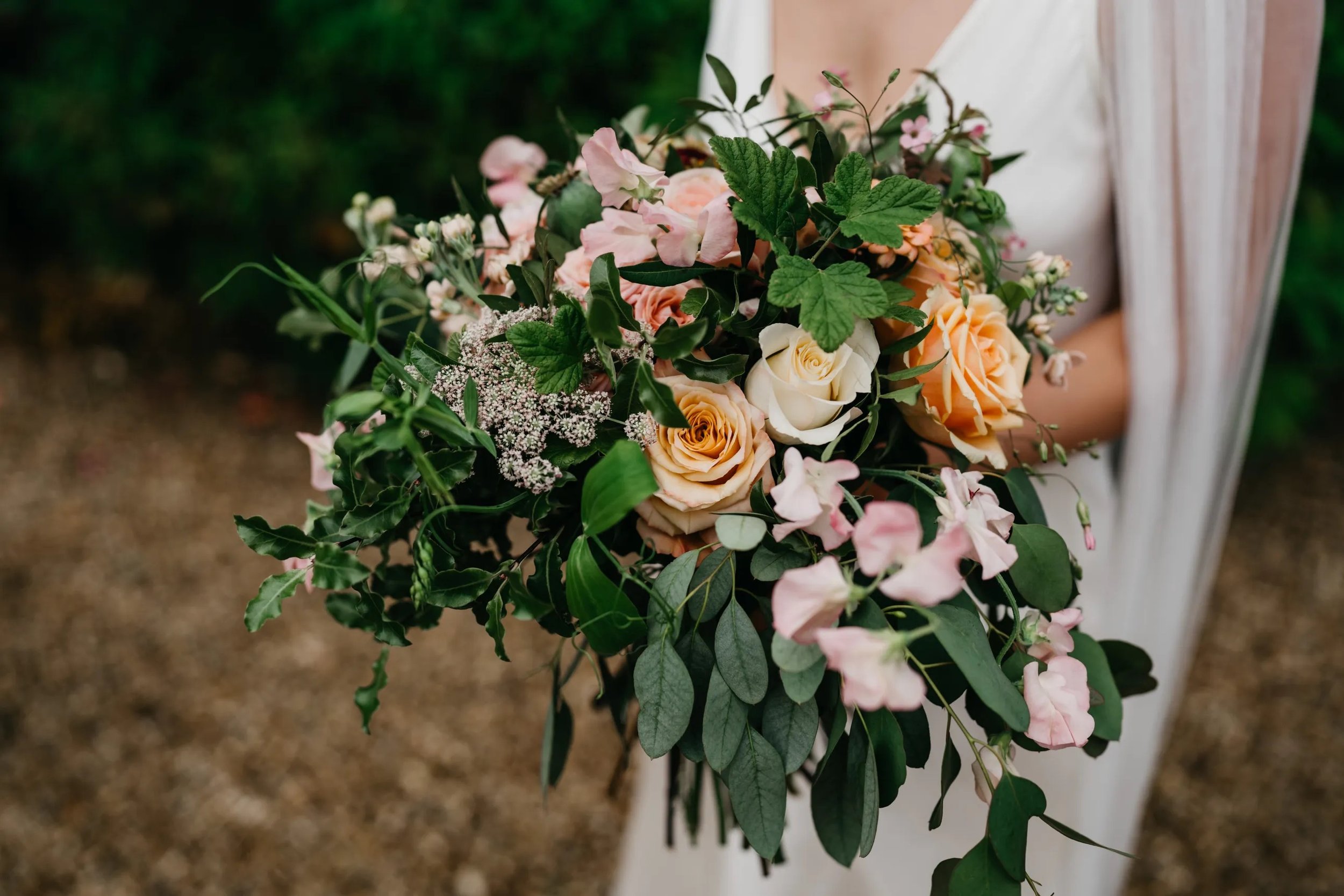  A close up image of a bride holding her large bridal bouquet, which is seasonal and looks natural with the soft pink and neutral florals amongst the greenery and foliage.  Photo by: Ed Godden @edgodden 