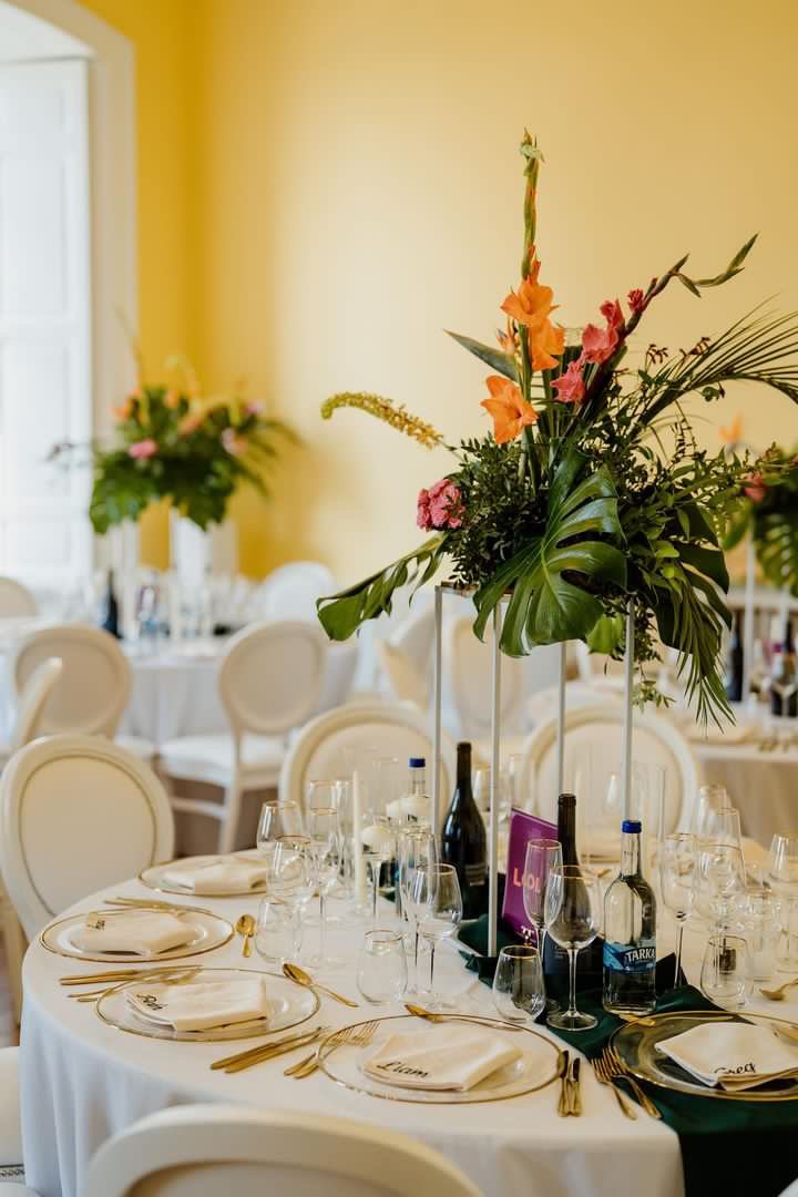  Large leaf foliage has been used to add fun and interest to the wedding table arrangement. The floral display is placed on a stand so wedding guests can talk across the table. Height and pops of colour also come from the individual stems.   Photo by