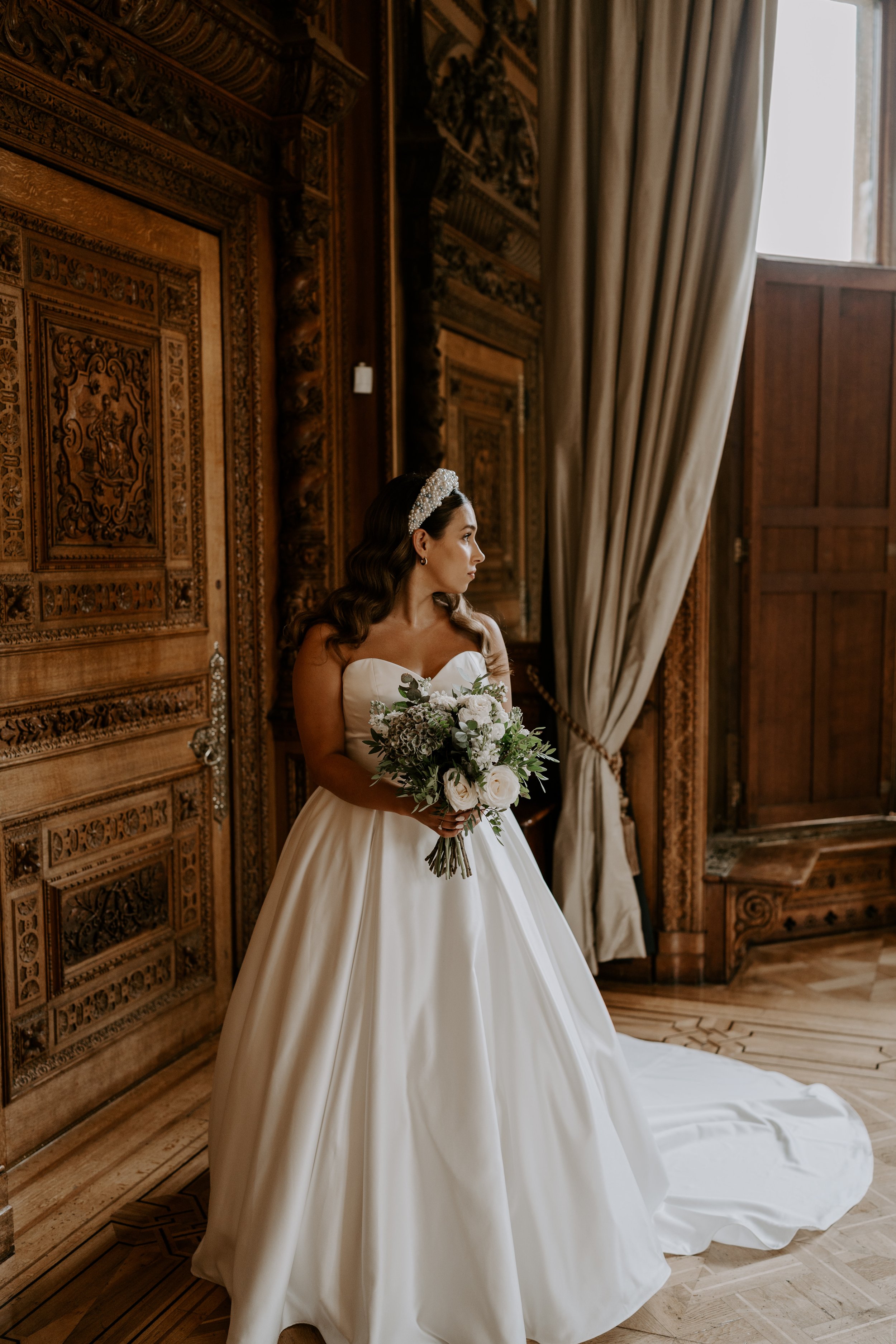  A stylish hand tied bouquet is being held by the bride as she stands in a grand wood panelled room. The brides simplistic palette makes a bold statement as the modern wedding bouquet is filled with white flowers and greenery.  Photo by: Marta D Phot