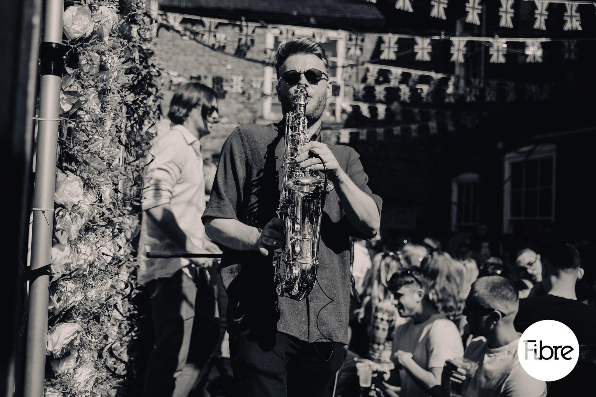  Black and white image of cool sax player entertaining wedding guests outside in the sunshine.    Photo by: Noah Rushbridge   