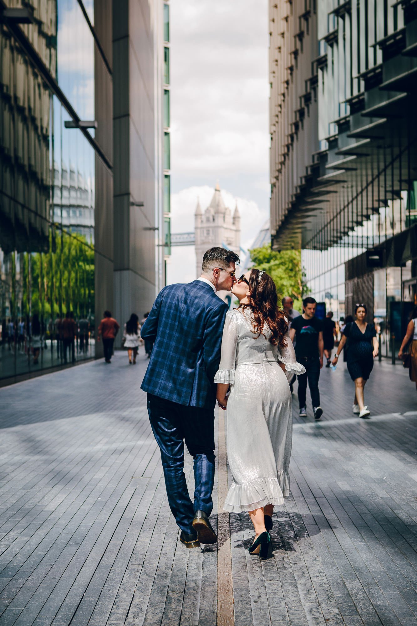 A natural moment captured by the non intrusive, photo ninja wedding photographer who doesn’t miss a detail. Bride and groom share a kiss as they are walking away from the photographer hand in hand, outside, up the street in between tall buildings. 