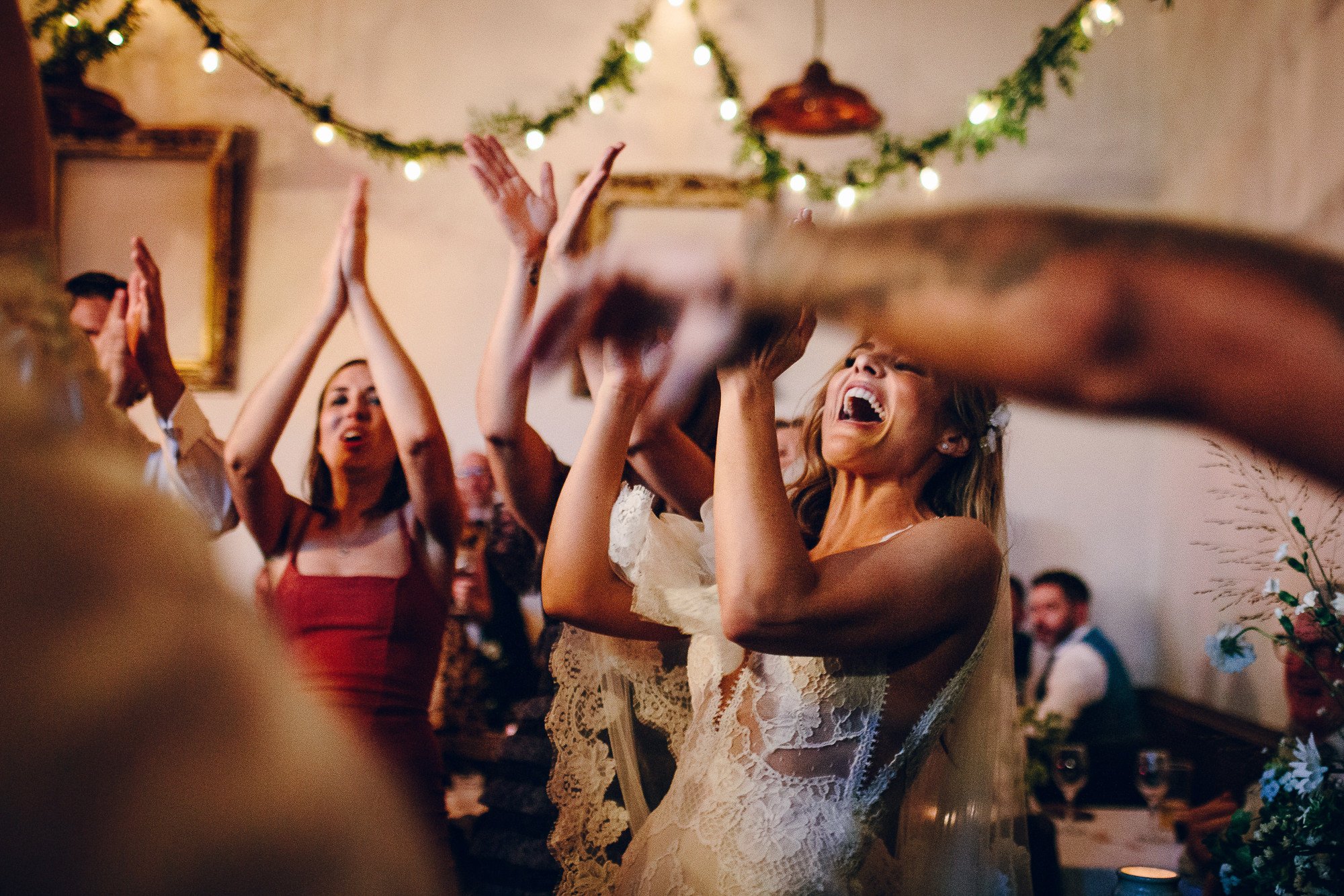  A wonderful action shot taken by the wedding photographer of the bride stood up laughing and clapping along with other wedding guests during the evening reception. 