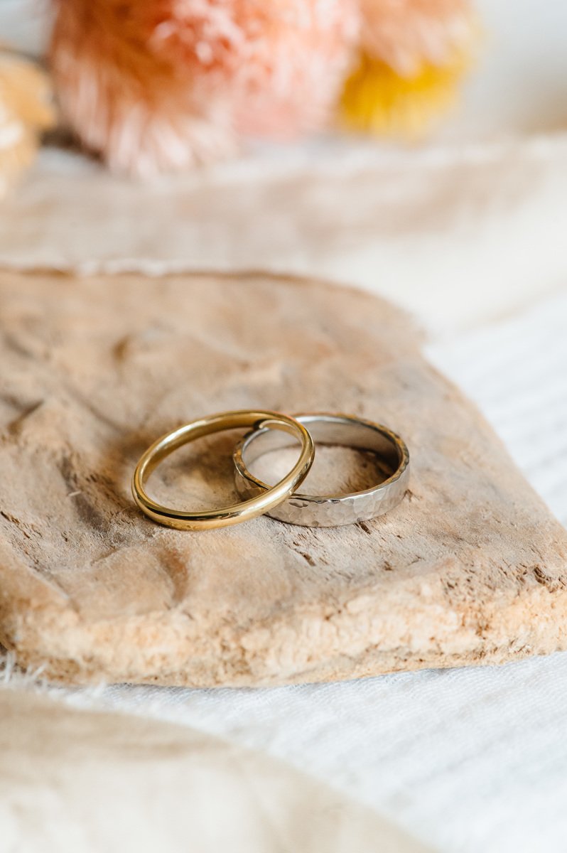  Two handmade wedding rings.   A slim gold wedding band is displayed angled on top of a wider hammered silver wedding ring.  Photo by: Fiona Kelly 