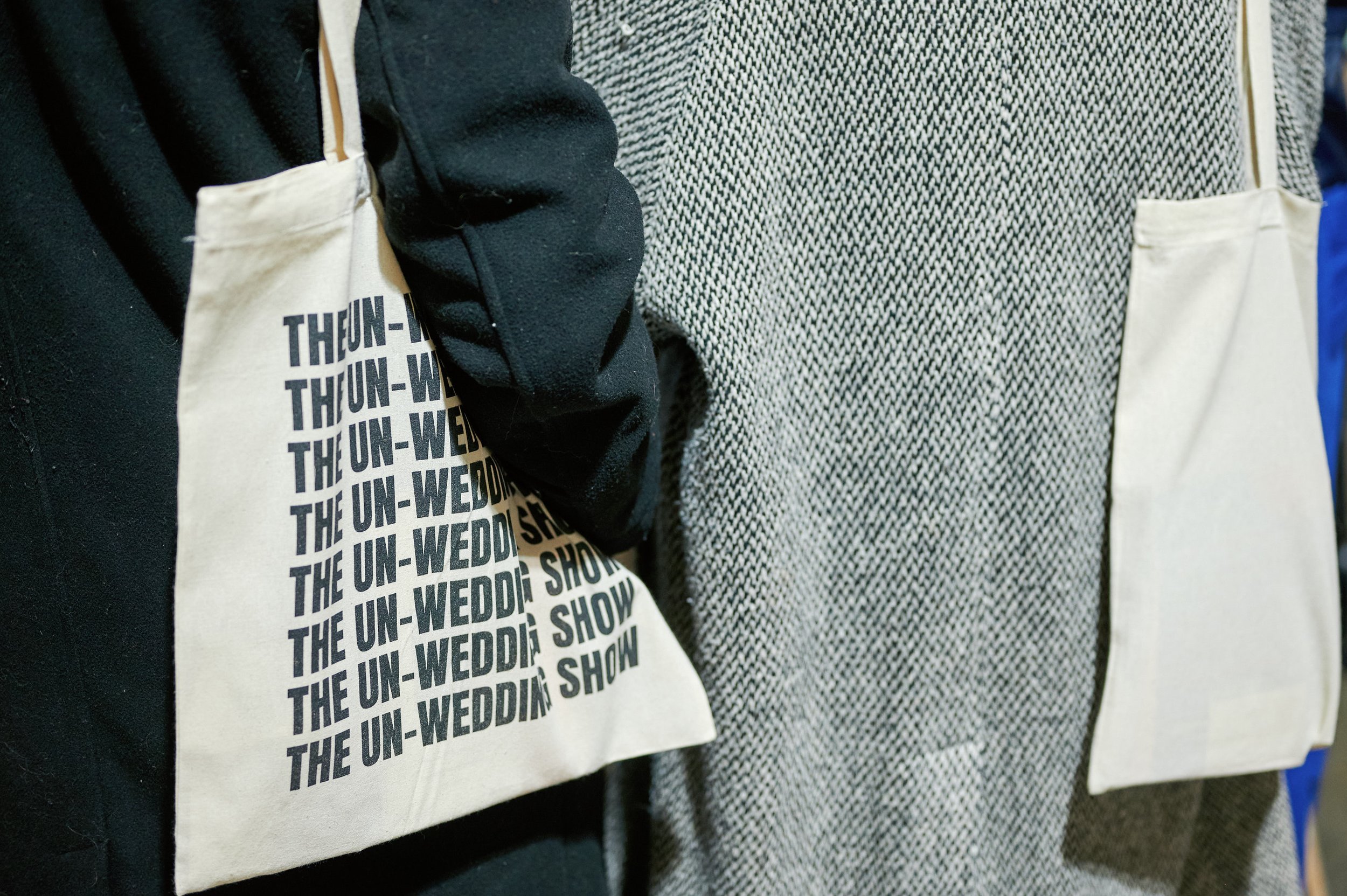  A close up of a person holding a cotton tote bag that says ‘THE UN-WEDDING SHOW’ in black print. 