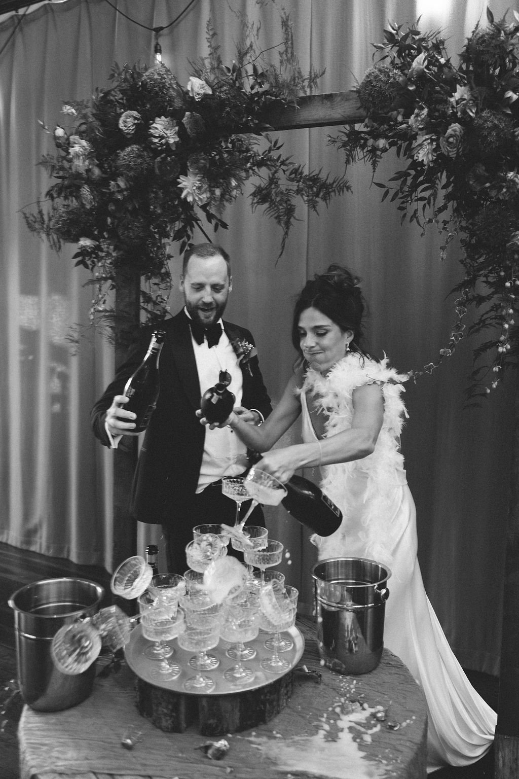 An awesome black and white image of the bride and groom as their champagne tower collapses whilst the bride is pouring the champagne. The wedding photographer has captured the authentic moment perfectly. 