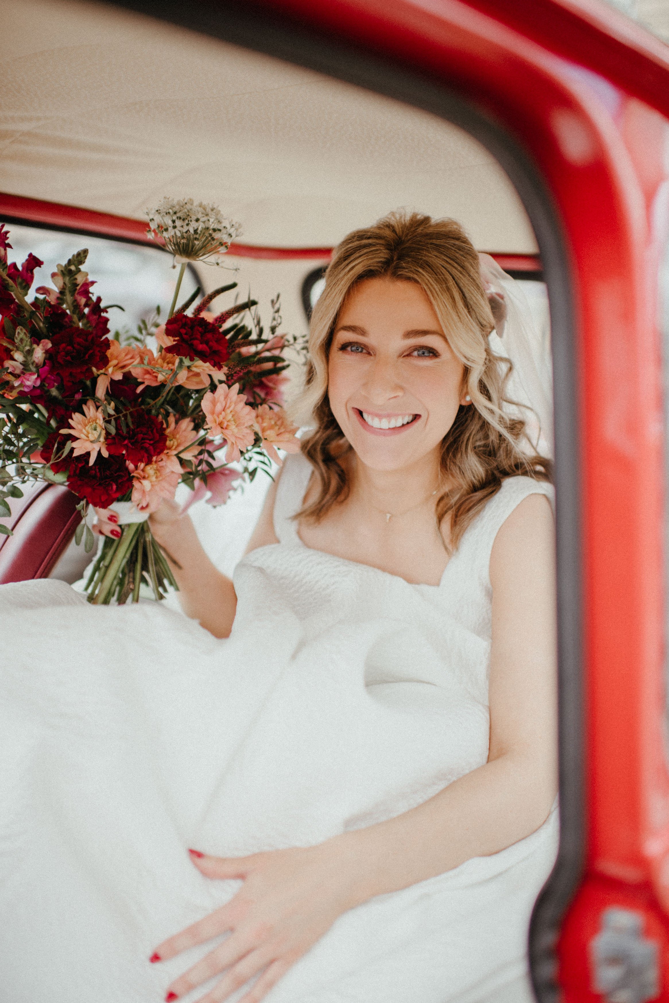  Modern wedding florals can be seen in the autumnal bridal bouquet, held by the bride who is sat in the back of a red car.  Photo by Lisa Devine Photography 