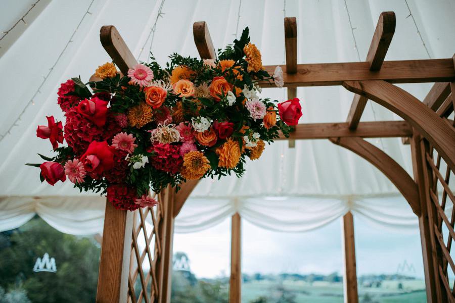  Various flowers in bright pinks and oranges look fun and modern in this wedding floral installation, which is displayed on the corner of a wooden frame.   Photo by Pocket Square Photography 