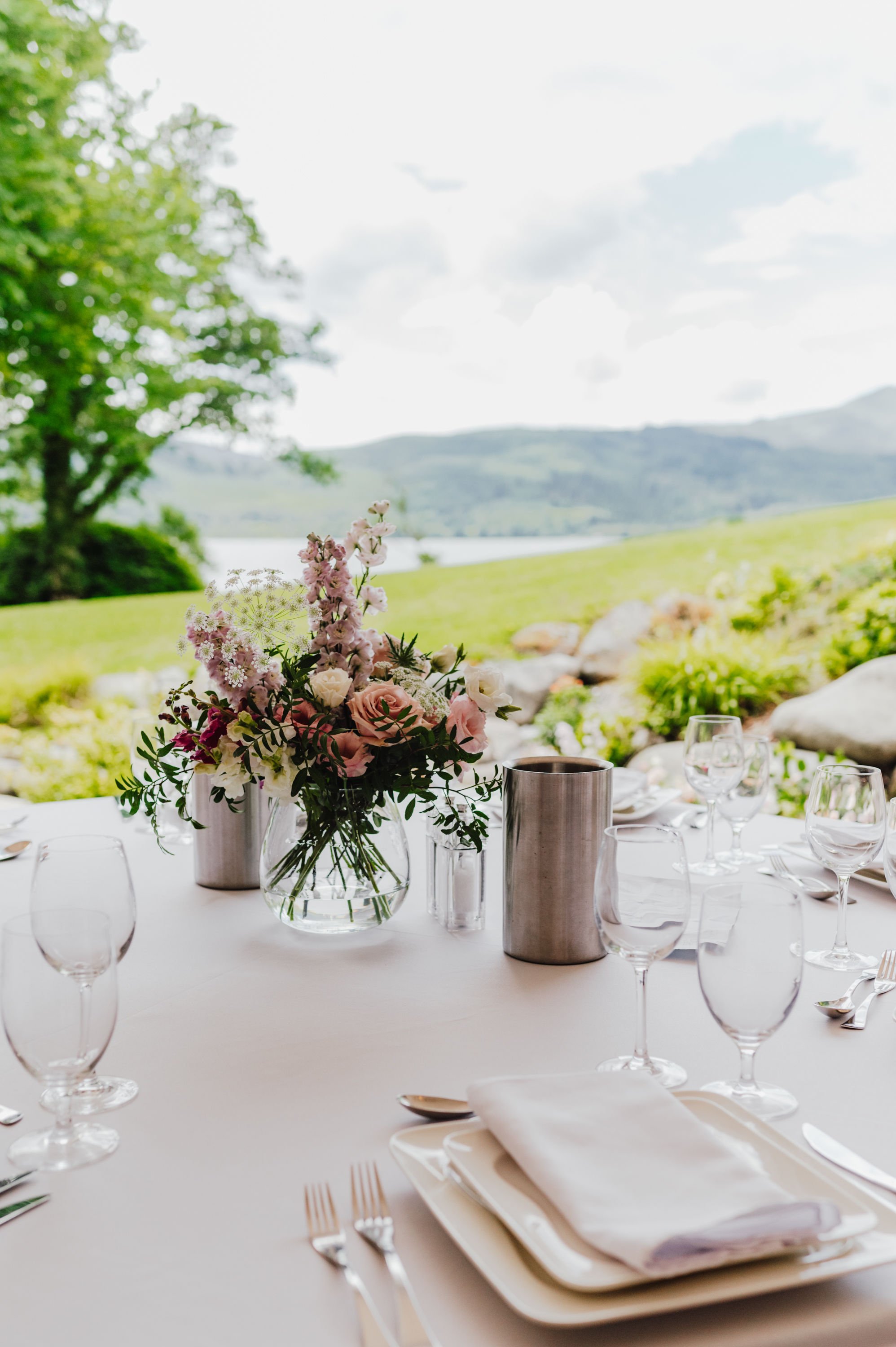  The carefully thought out wedding florals tonally reflect the outside scenery.  A beautiful, natural looking floral centrepiece in muted pink florals at various heights and green foliage, adds personality and interest to the tables which have been l