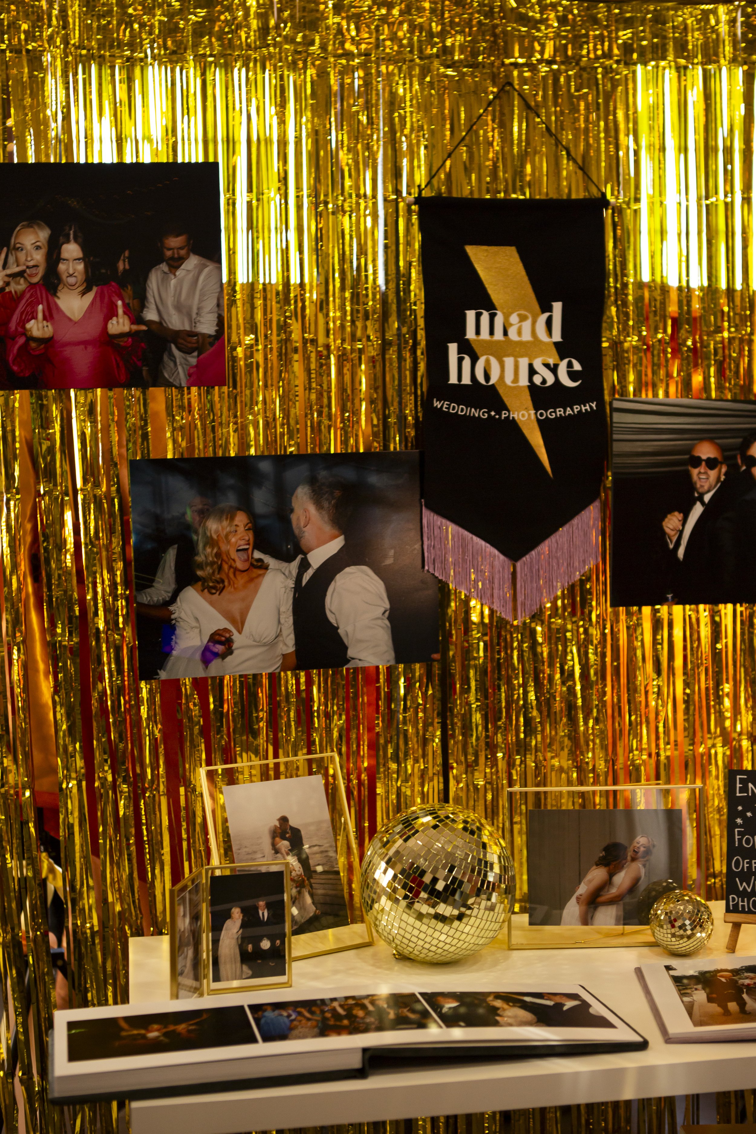  Beautiful velvet banner with alternative photographers MAD HOUSE WEDDINGS name hung alongside their quirky style wedding photographs displayed against a gold streamer wall. 