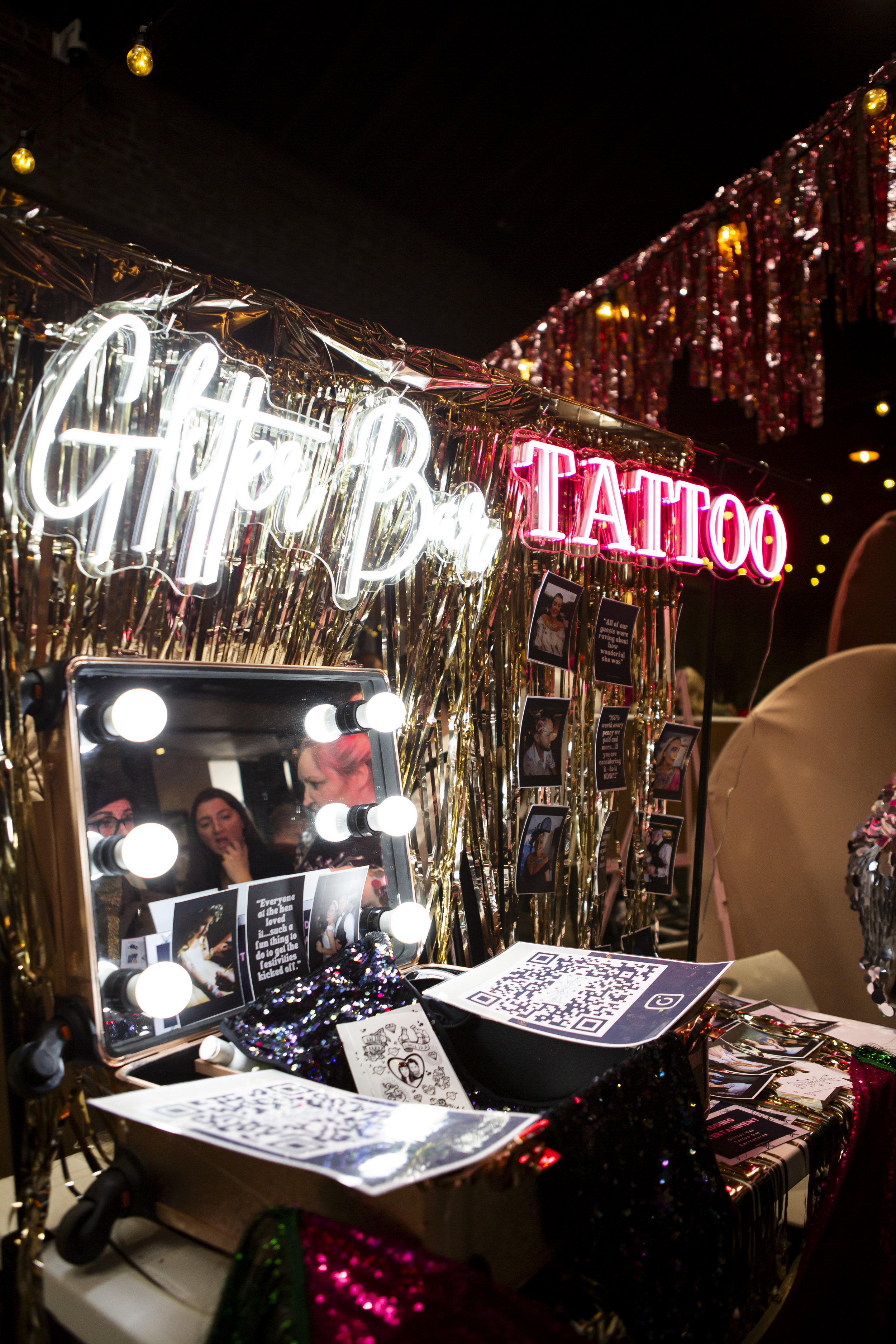  Stunning wedding setup showcased with neon GLITTER and TATTOO signs displayed against gold fringing wall alongside a Hollywood mirror with lightbulbs. 