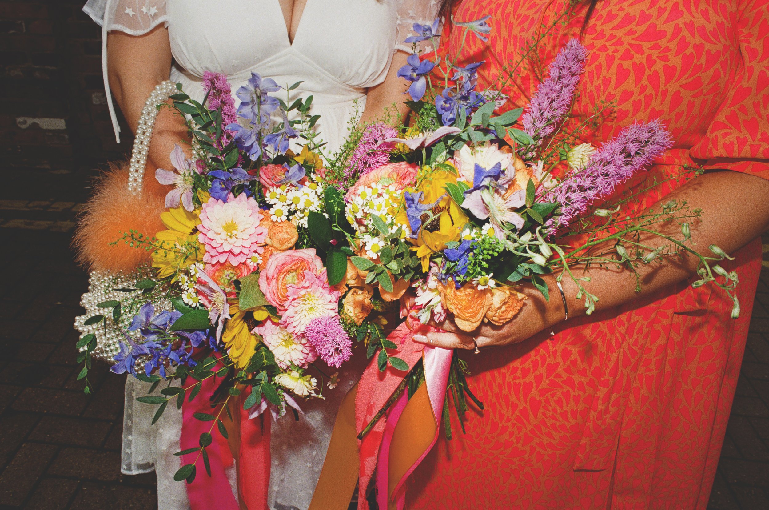  A close up image of the bride’s and bridesmaids fun wedding bouquets.  Both the hand-tied bouquets are unique but have similar bright, modern flowers incorporated and tied with bright pink &amp; orange ribbons.  Photo by Belles Confetti Photography 