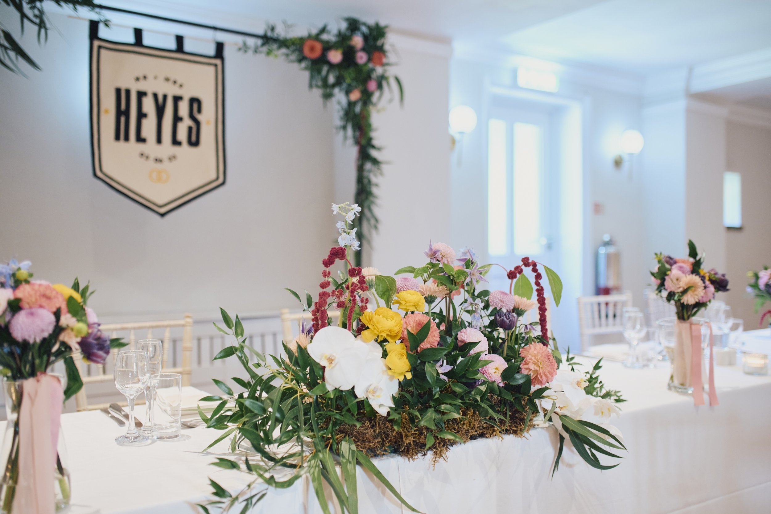  Modern, spring wedding floral  decoration on the top table. The corner of a frame behind where the bride and groom are sitting has also been decorated with flowers and foliage which compliment the florals used on the tables.   Photo by Wedding Day P