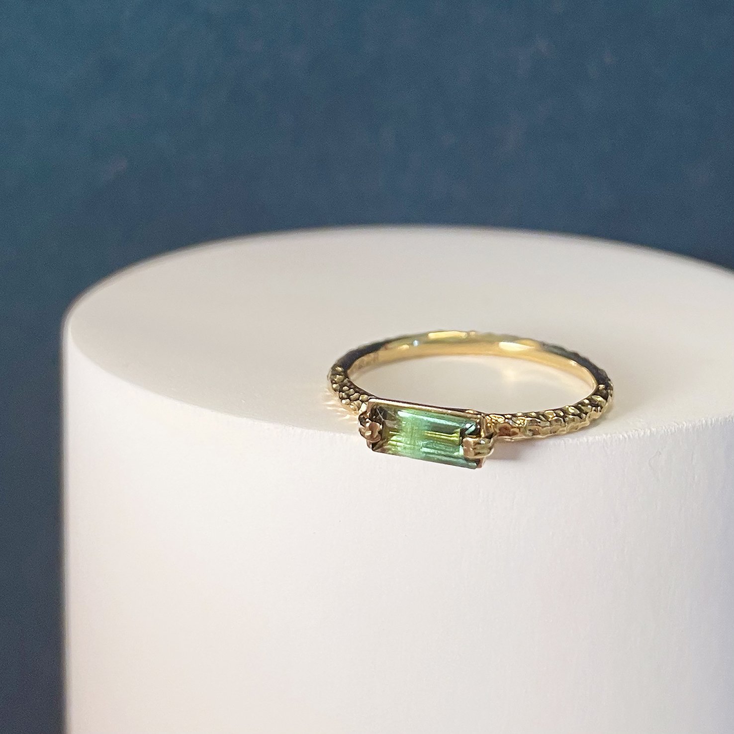  A narrow gold, textured wedding band with a green rectangle stone set on top. 