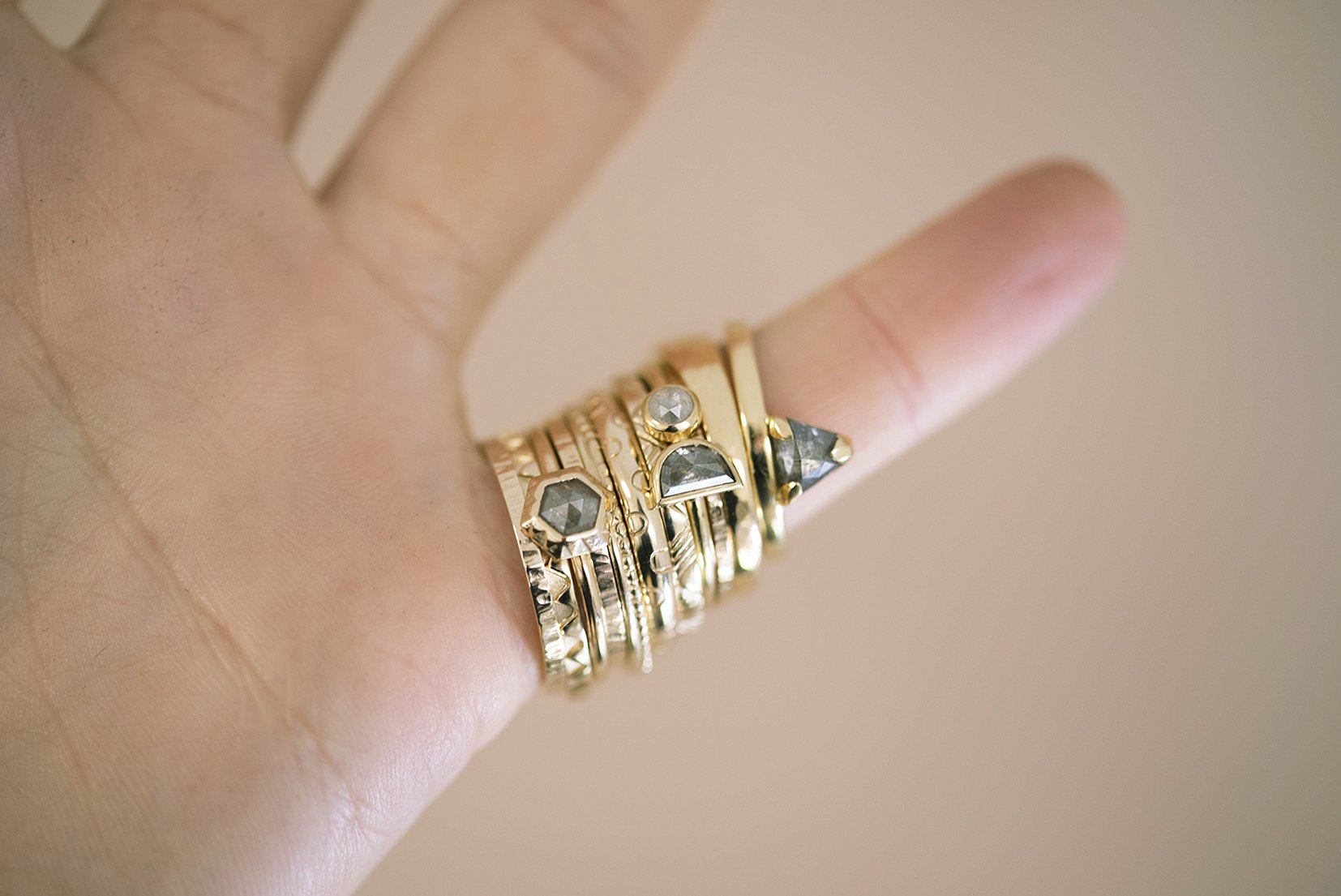  Multiple wedding rings stacked and displayed on one finger. The modern gold rings are a mixture of widths and textures, some set with stones and some without. 