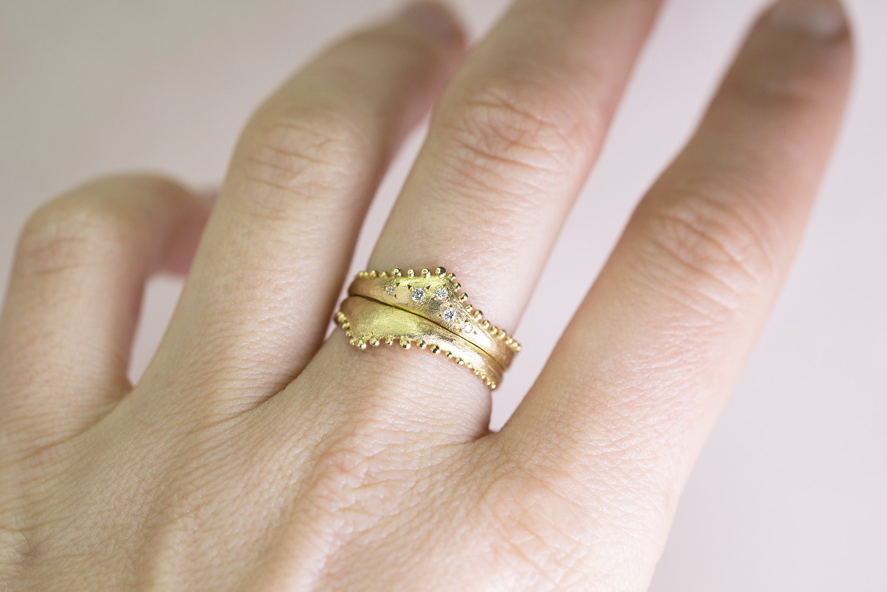  Two gold wishbone shaped rings displayed stacked so the points create a diamond on the finger.   The bottom ring is plain and worn as a wedding band, whilst the top one as the engagement ring has diamonds inset. 