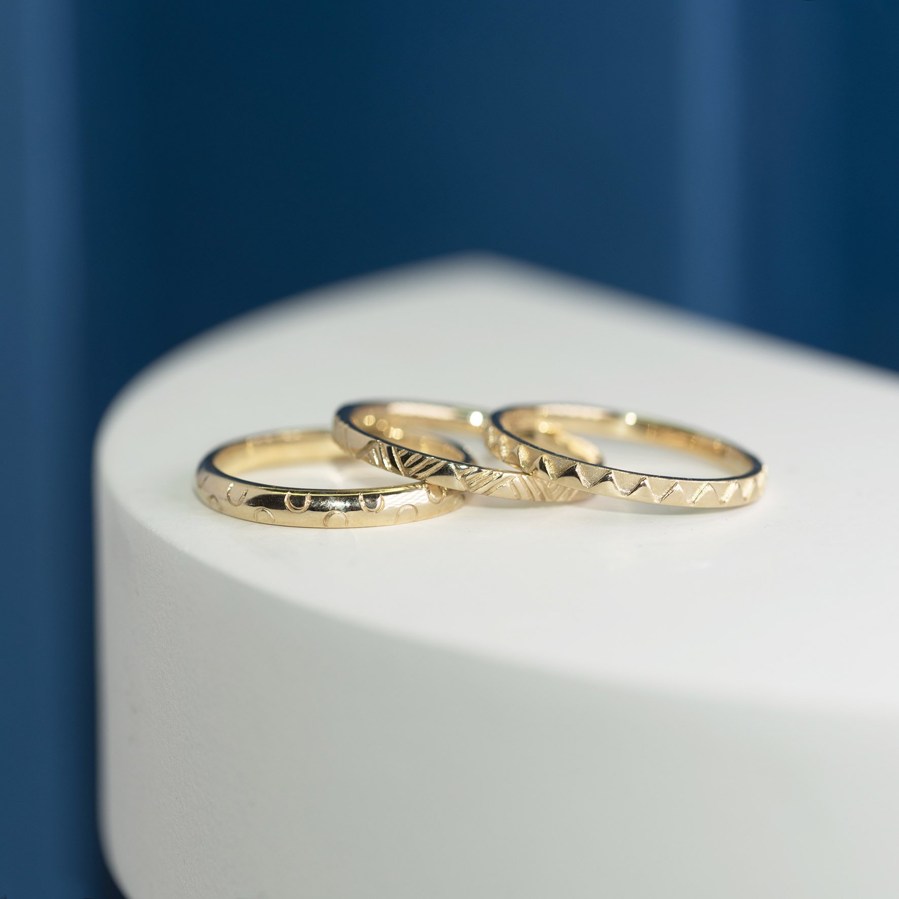  Three bespoke, slim, gold wedding bands all with slightly different subtle graphic patterns on the outside. 