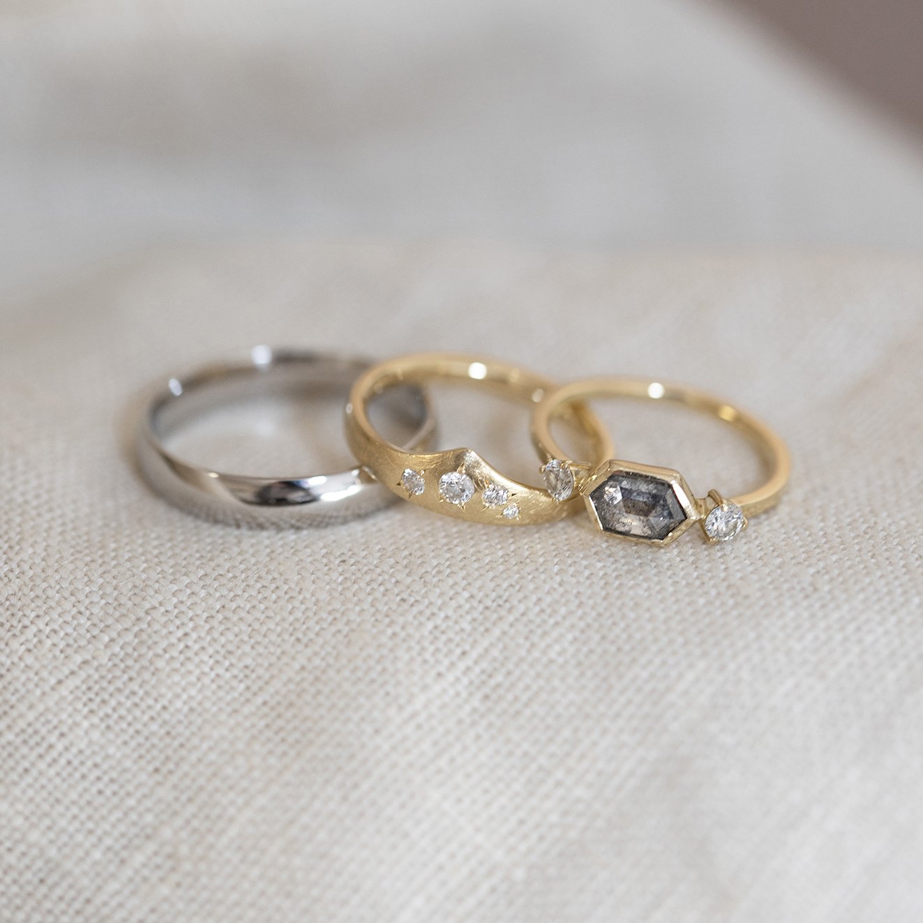  Three wedding rings. One plain silver wedding band, a diamond embellished wishbone shaped engagement ring and a modern, slim gold band with a bespoke stone shape set within it. 