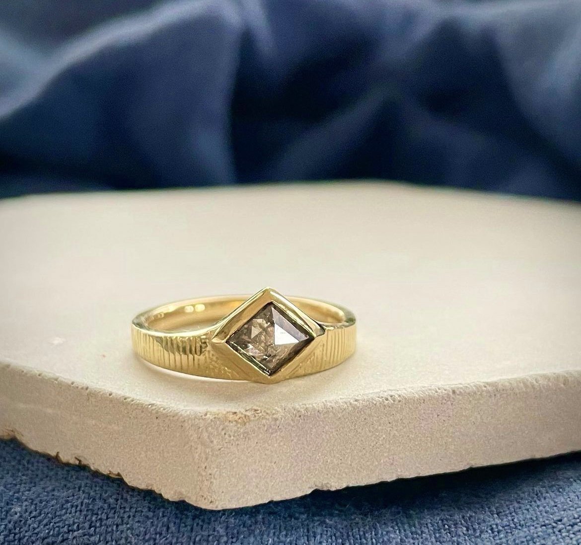  A modern bespoke wedding ring. The chunky, graphic textured gold band showcases a diamond shaped stone set within it. 