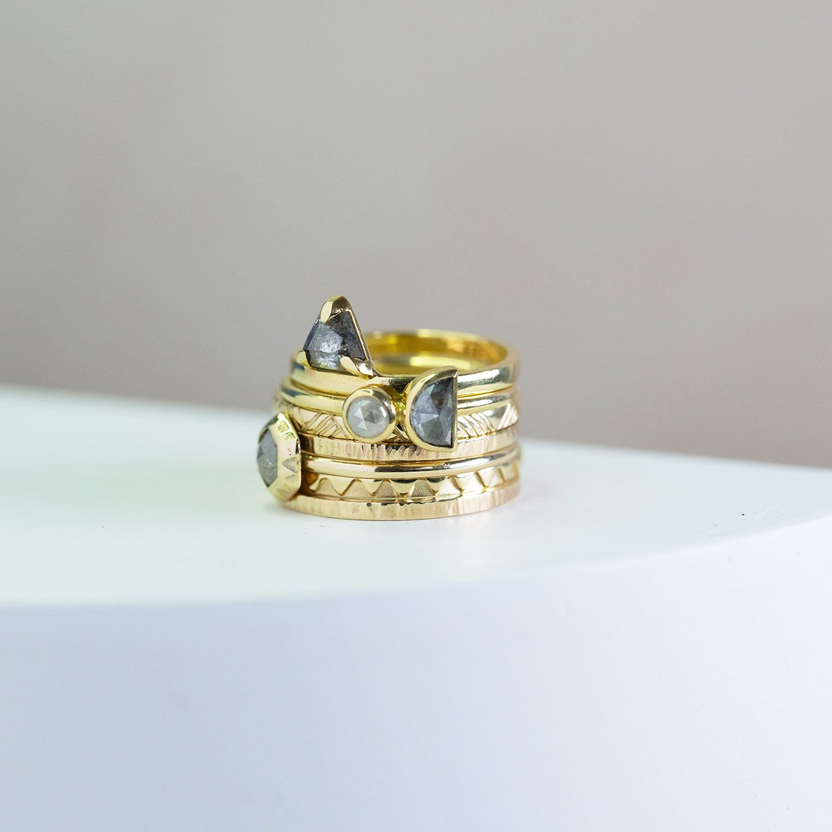  A stack of wedding bands and engagement rings, all with subtle graphic textures and patterns and some with modern, ethically sourced blue stones set in. 