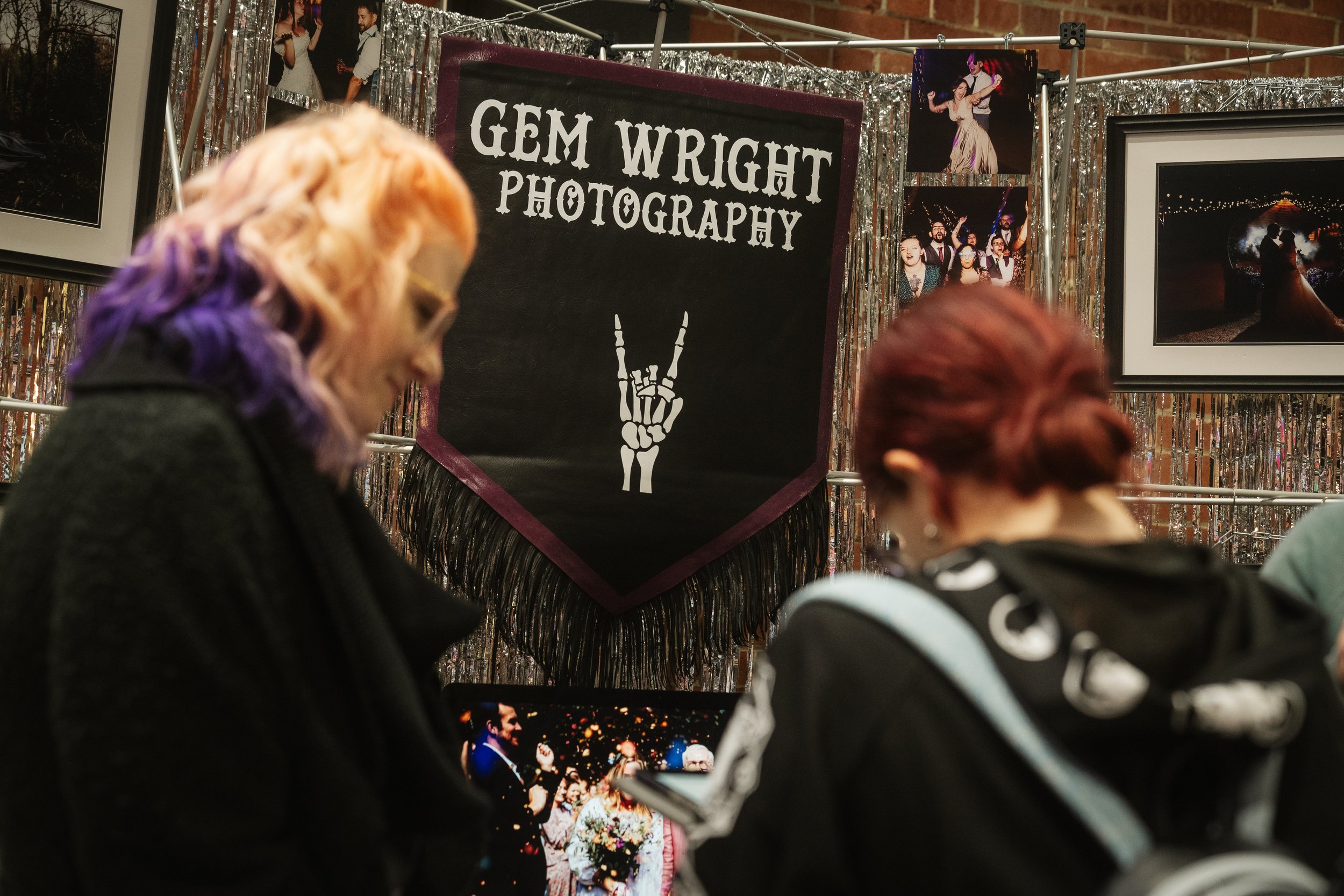  Alternative wedding photographer talking to attendees at The un-Wedding show in front of her cool banner with we rock skeleton fingers image.  