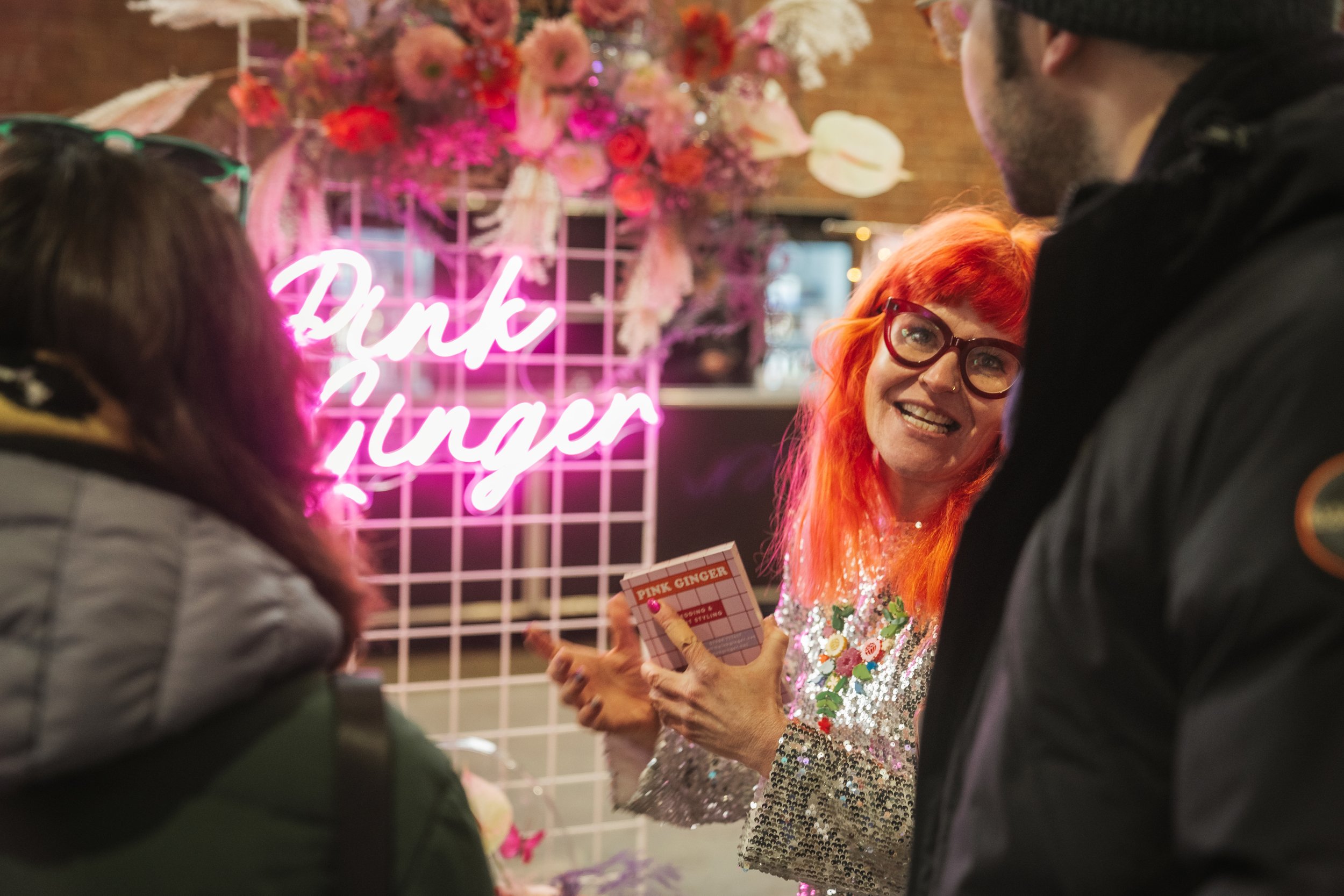  PINK GINGER bright pink neon on the stand behind the modern wedding florist who is chatting to attendees. 