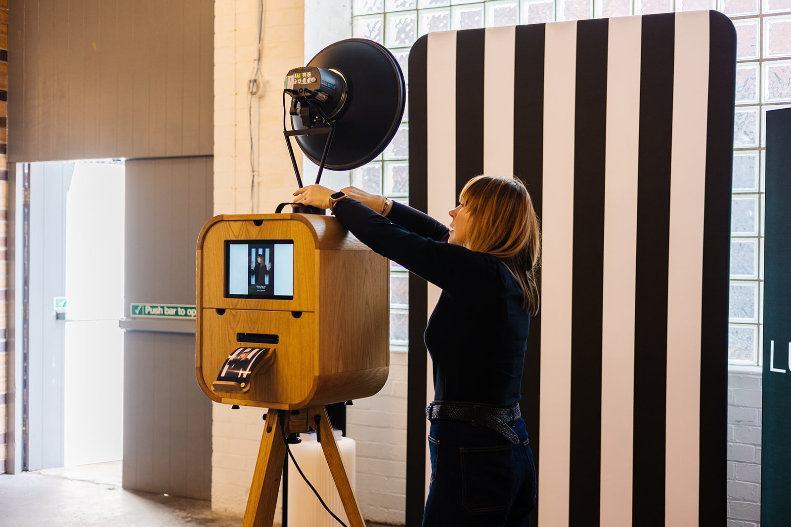  A woman setting up a cool wedding photo booth with a black and white stripey backdrop. 