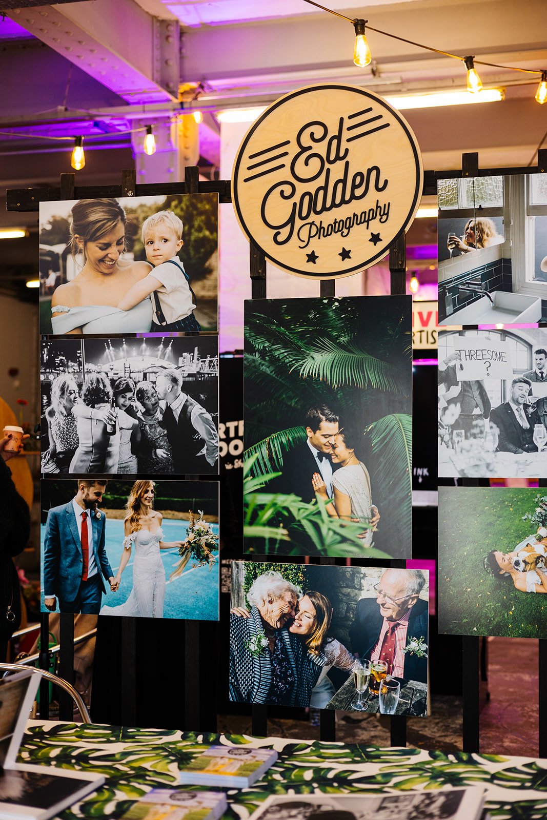  A modern photography stand at a wedding fair. There is a circular wooden sign that says Ed Godden Photography. 