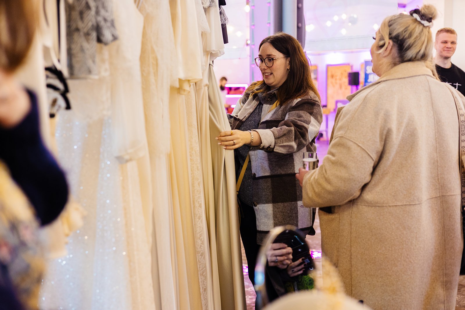  Attendees at a wedding fair browsing through rails of bridal gowns. 