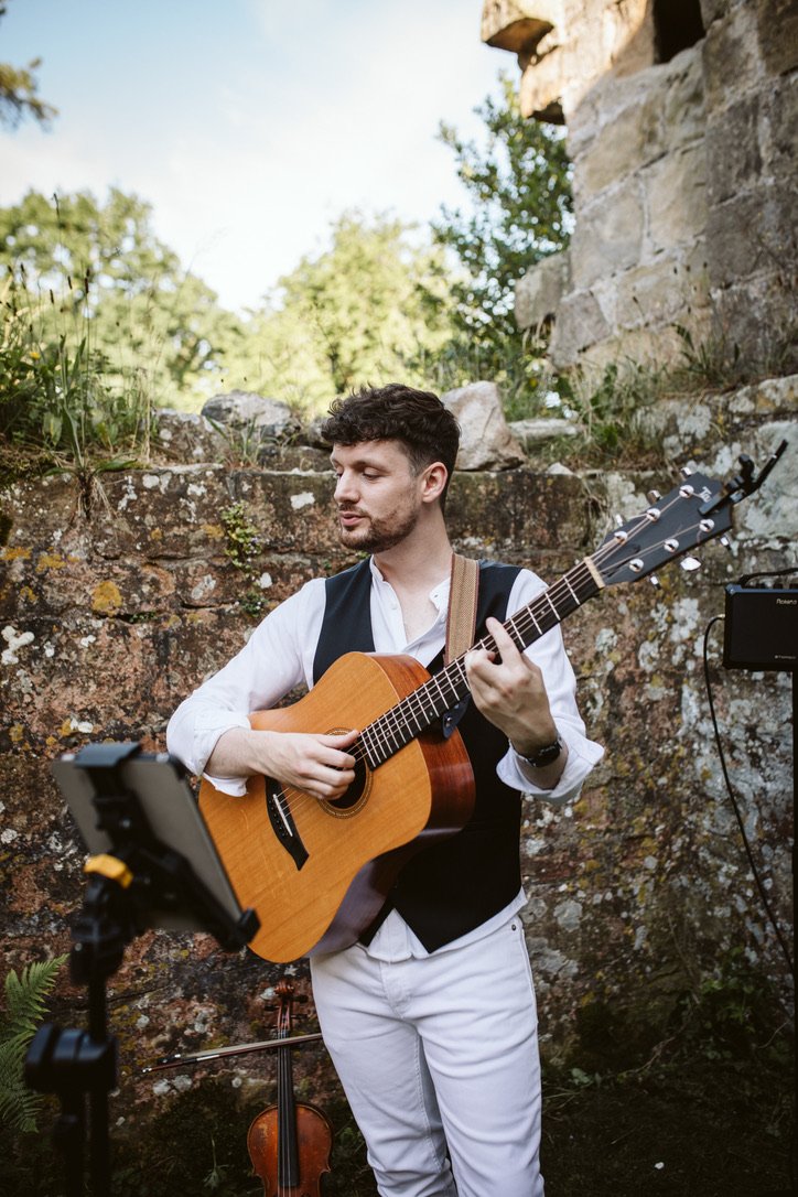 An acoustic guitarist playing outside during a wedding.
